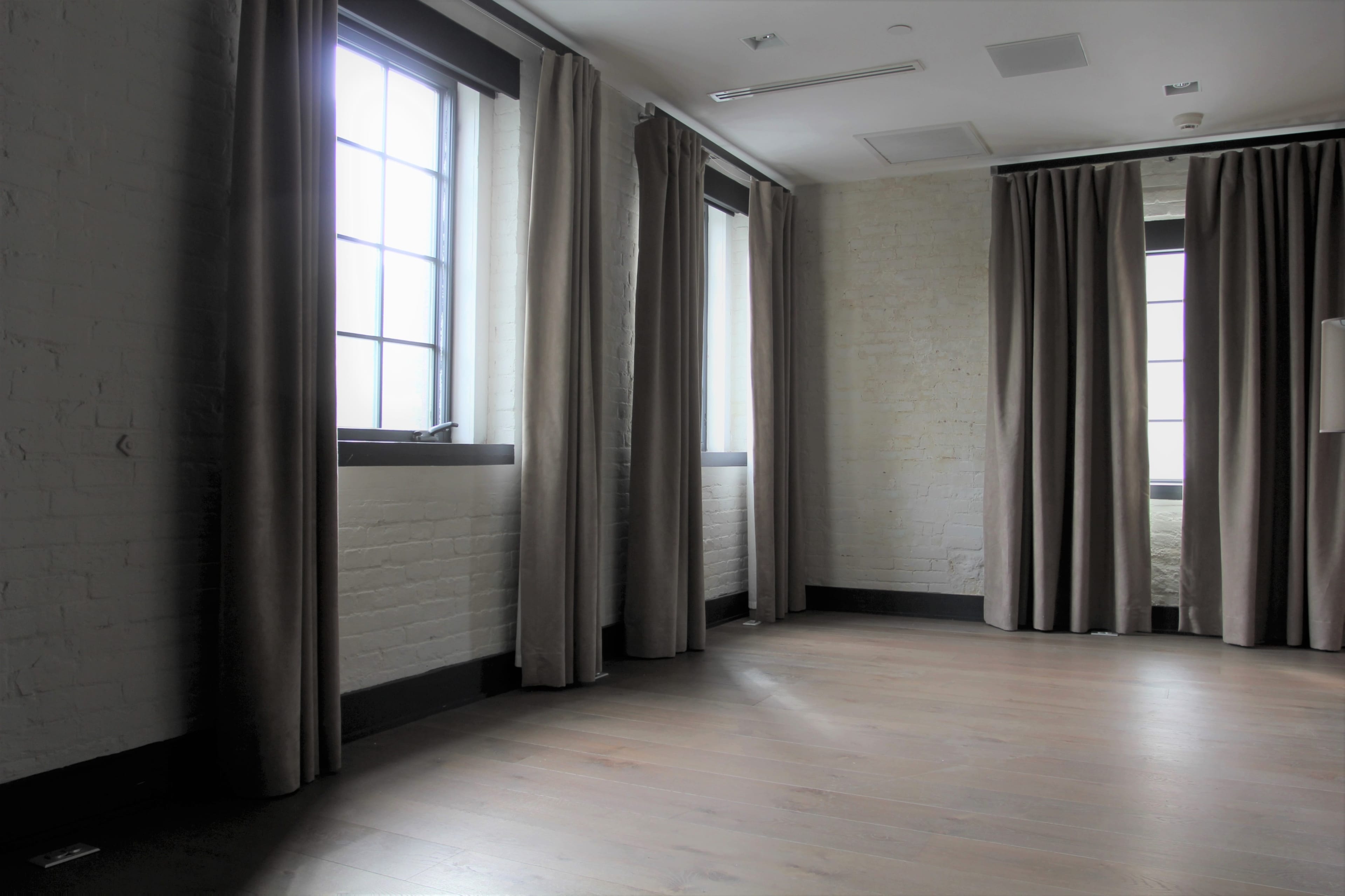 An empty room with two large windows, light-colored walls, and dark curtains.