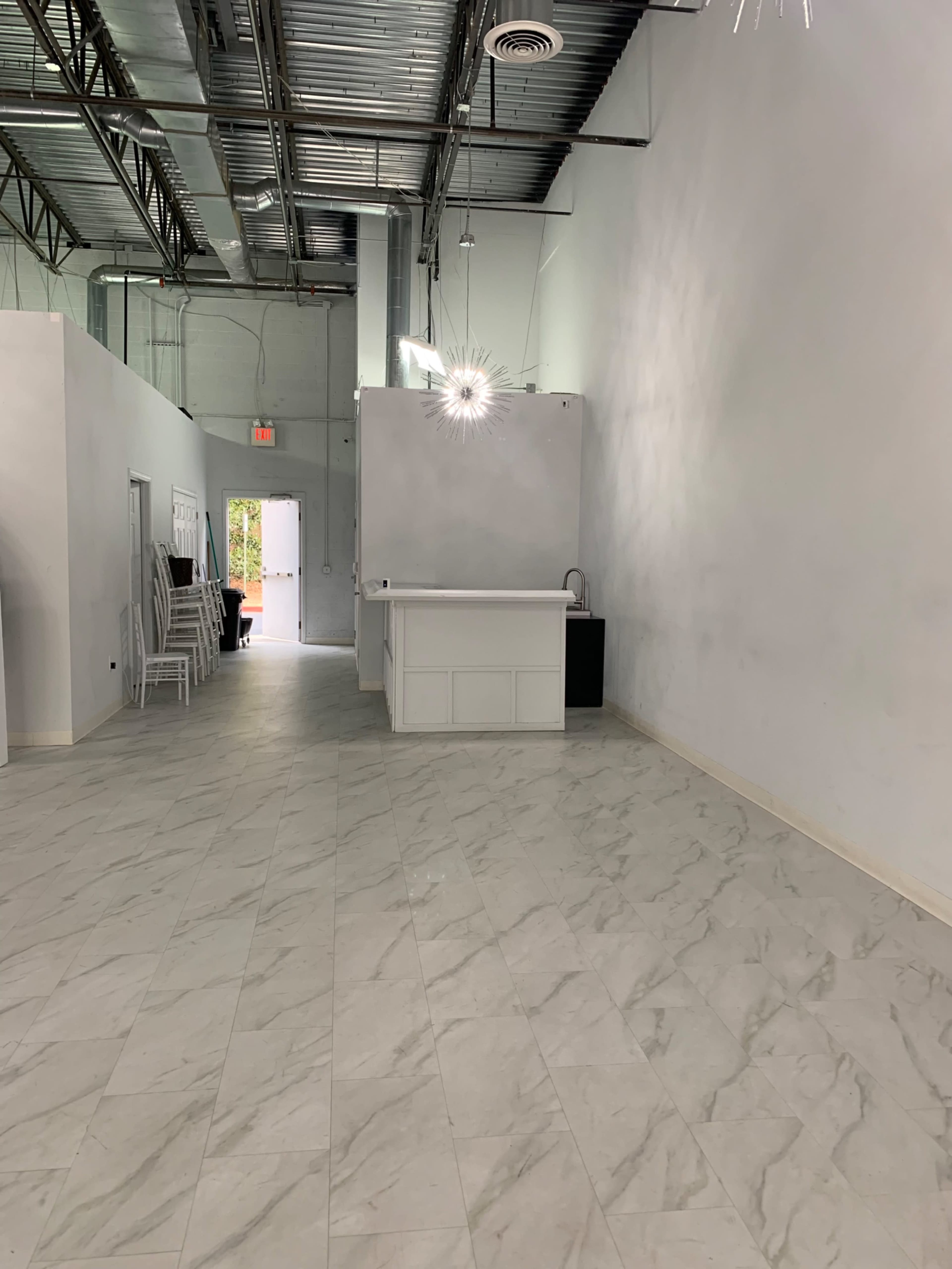 A spacious, empty interior with light-colored walls, tile flooring, and a reception area at one end.