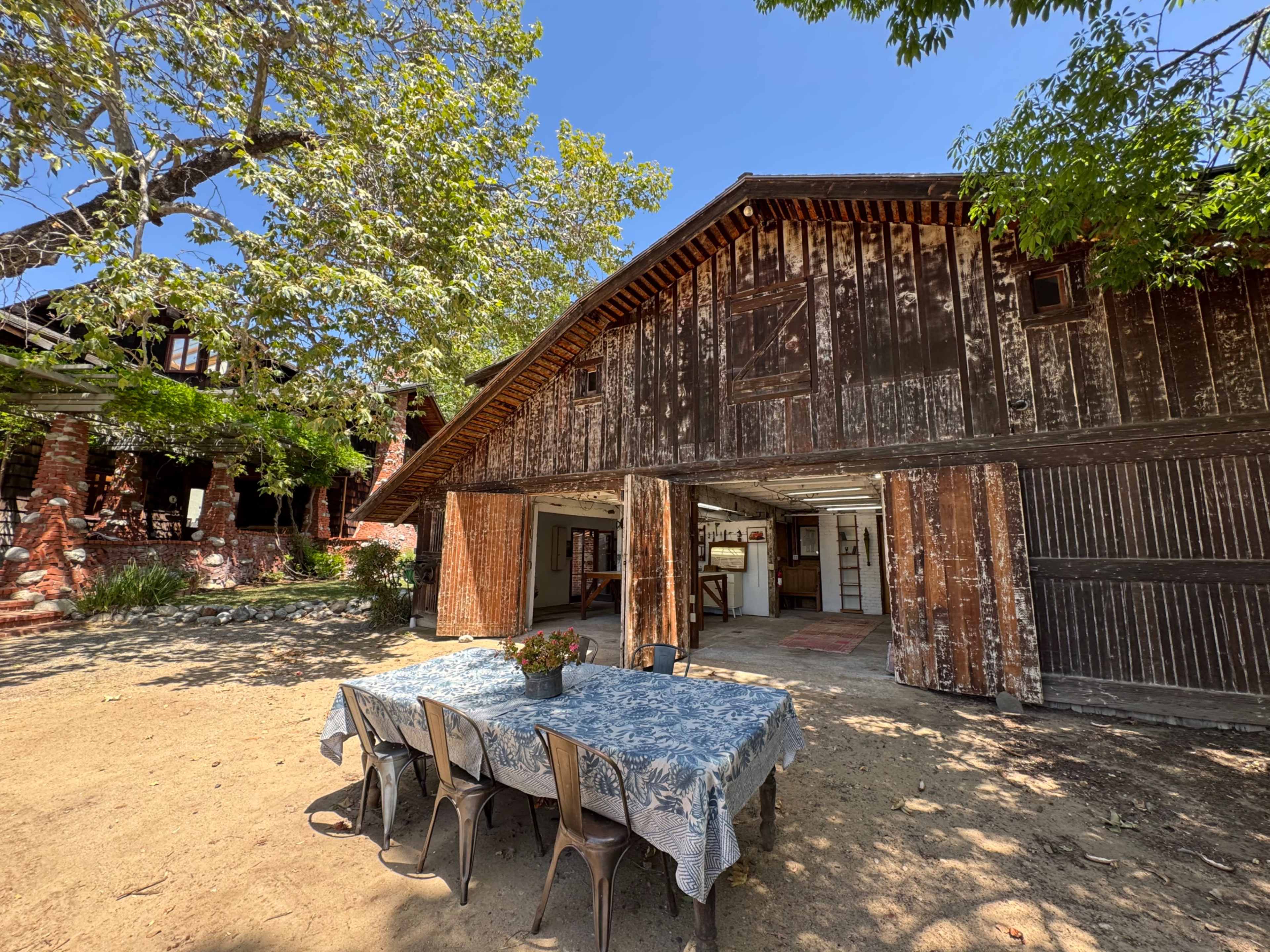 A weathered barn stands adjacent to a table set with chairs under a clear blue sky.