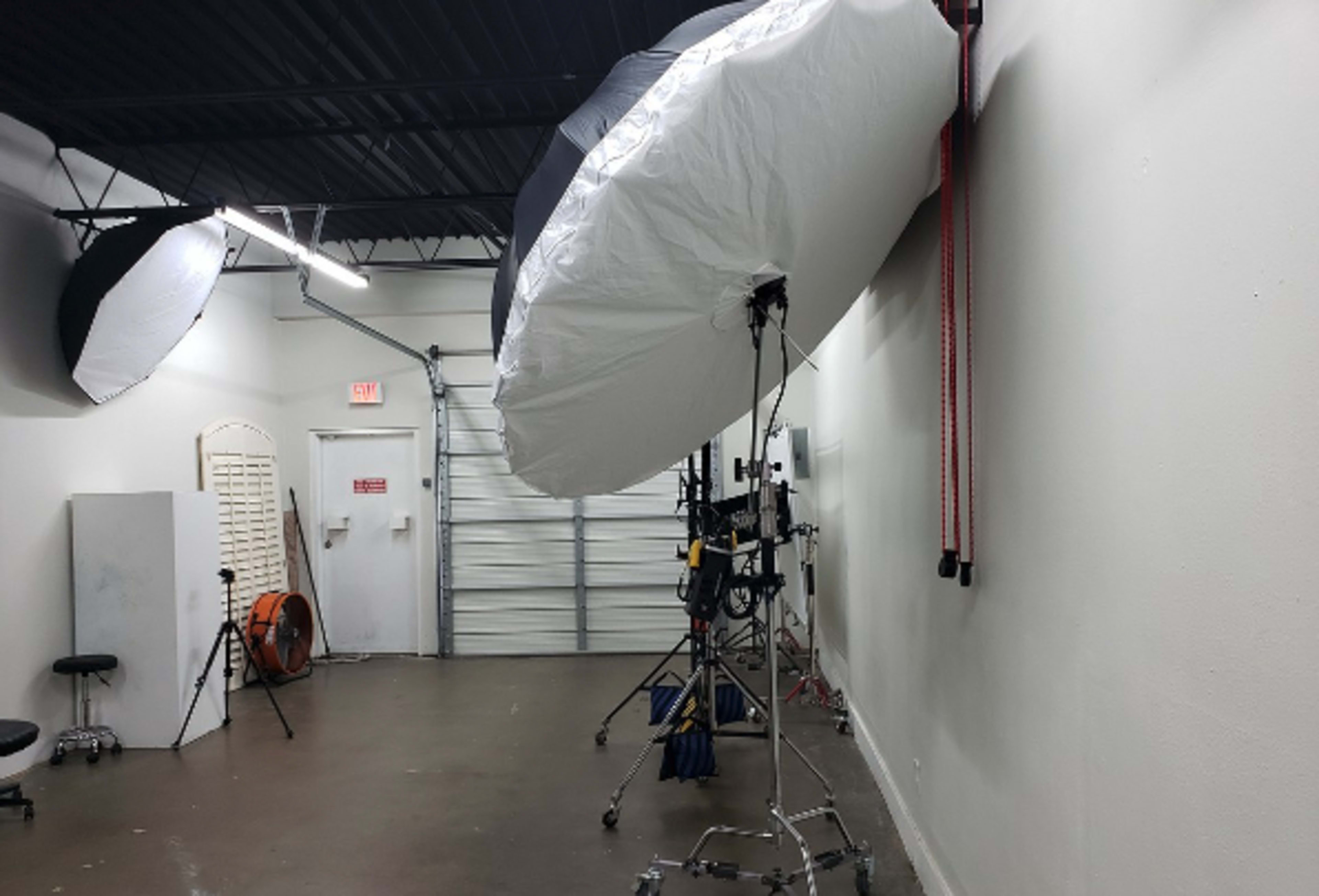 The image shows a photography studio with large softbox lights mounted on stands, a backdrop, and a garage door.