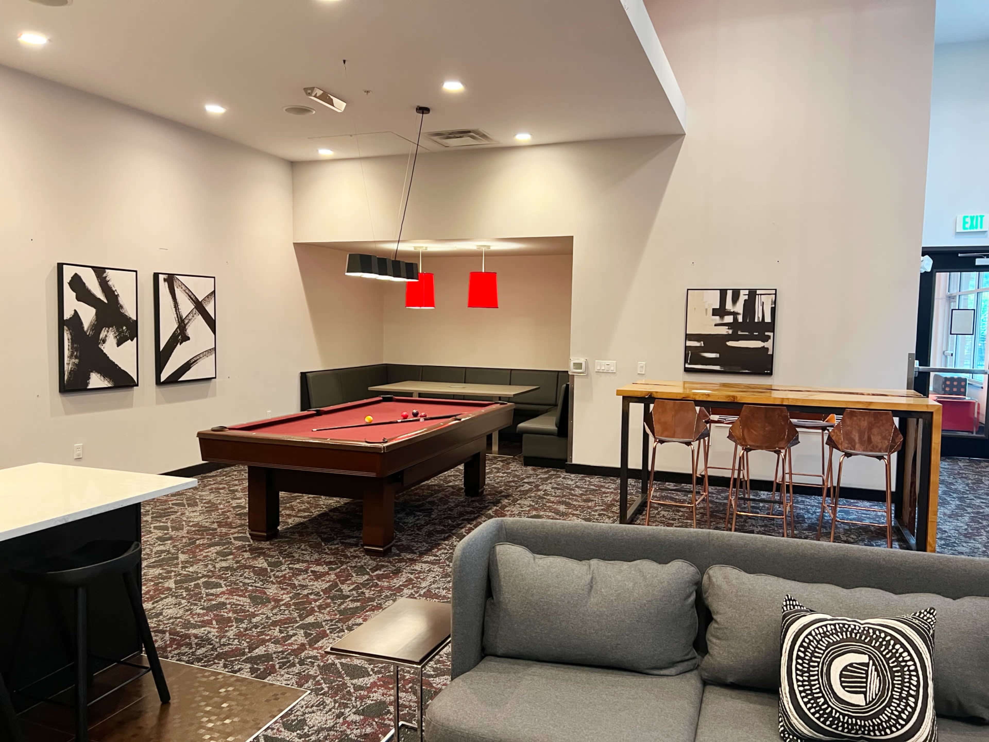A modern recreational room with a pool table, seating areas, and contemporary artwork on the walls.