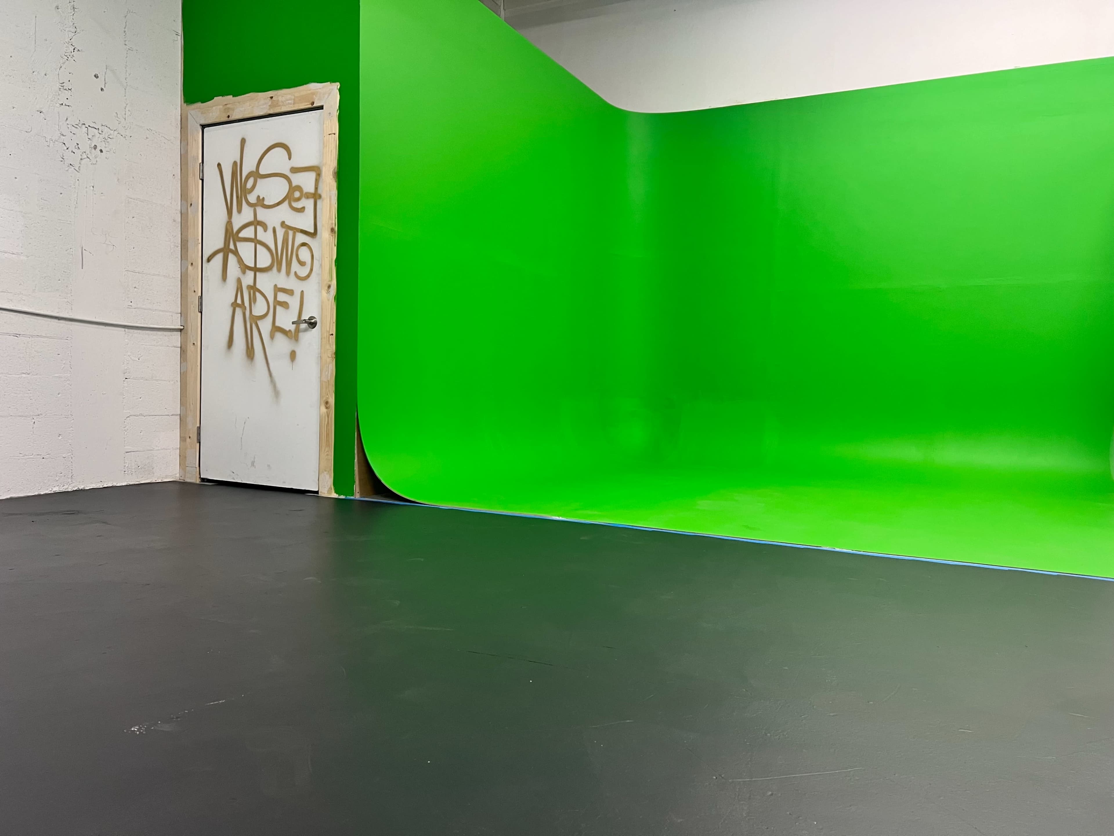 A studio space with a green backdrop and a door featuring graffiti.