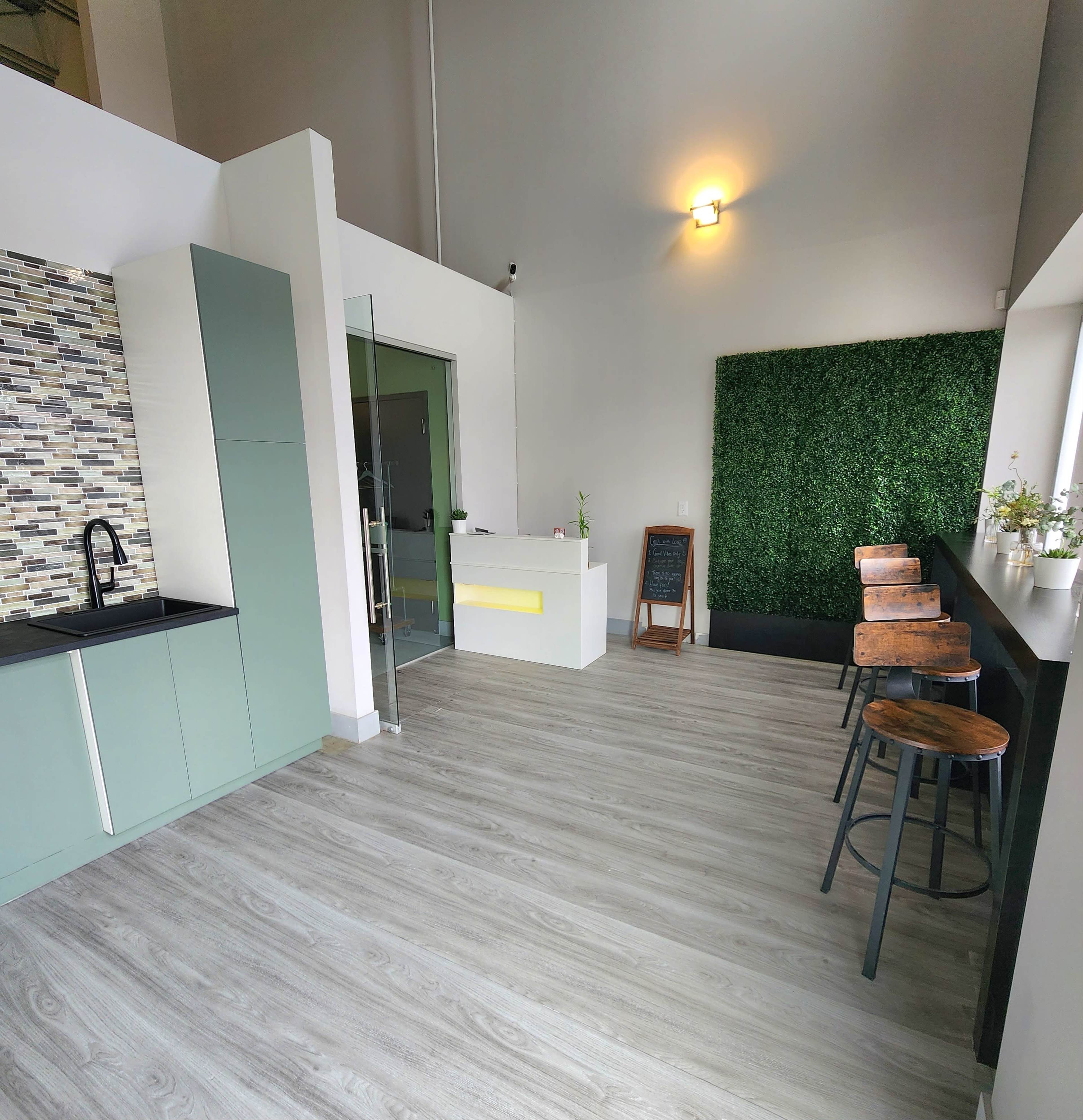 The image shows a modern interior space featuring a reception area with a green wall, bar seating, and an open layout with light wood flooring.