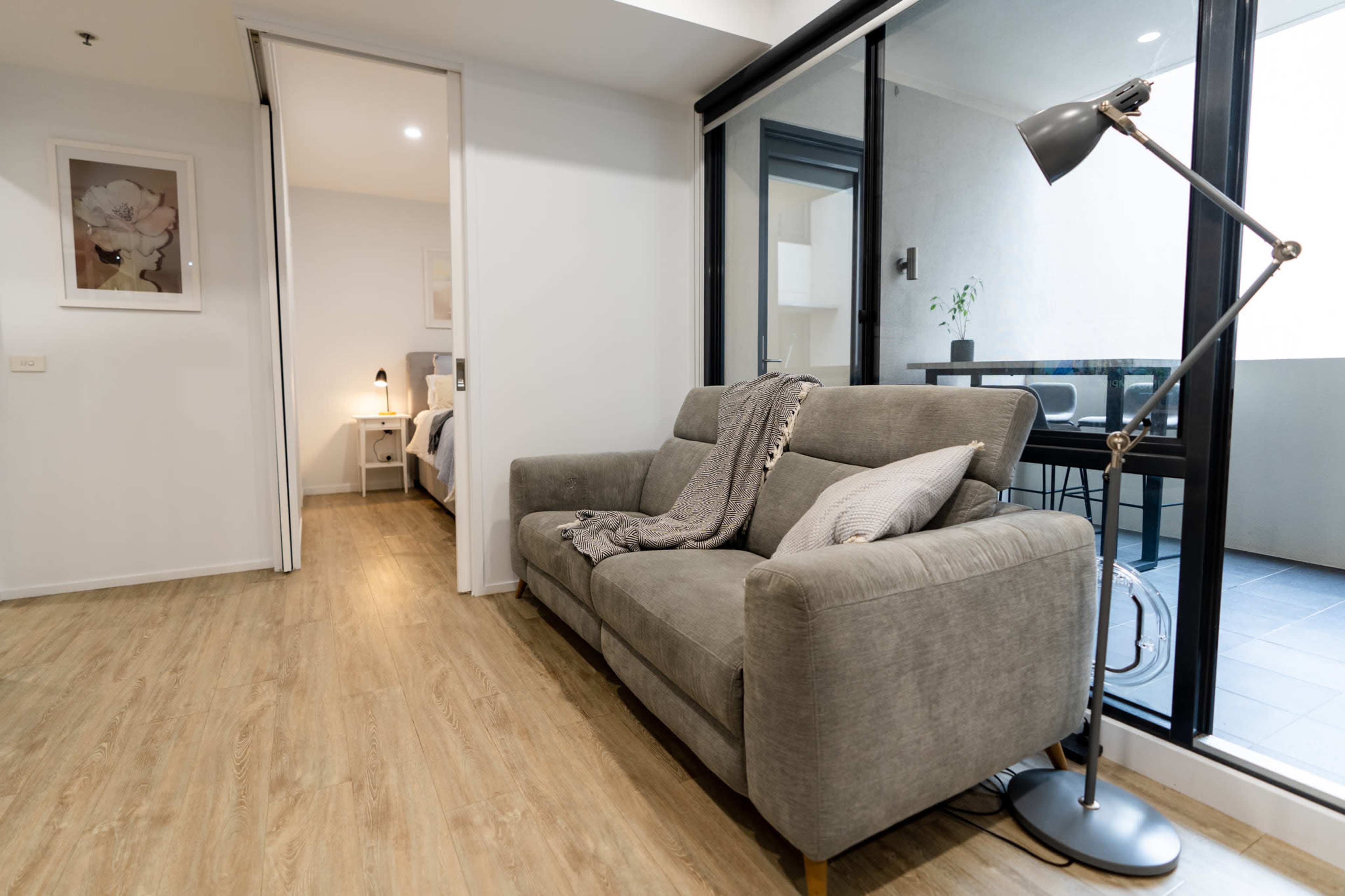 A gray sofa is placed in a modern, open living area with large windows and a view of a balcony.