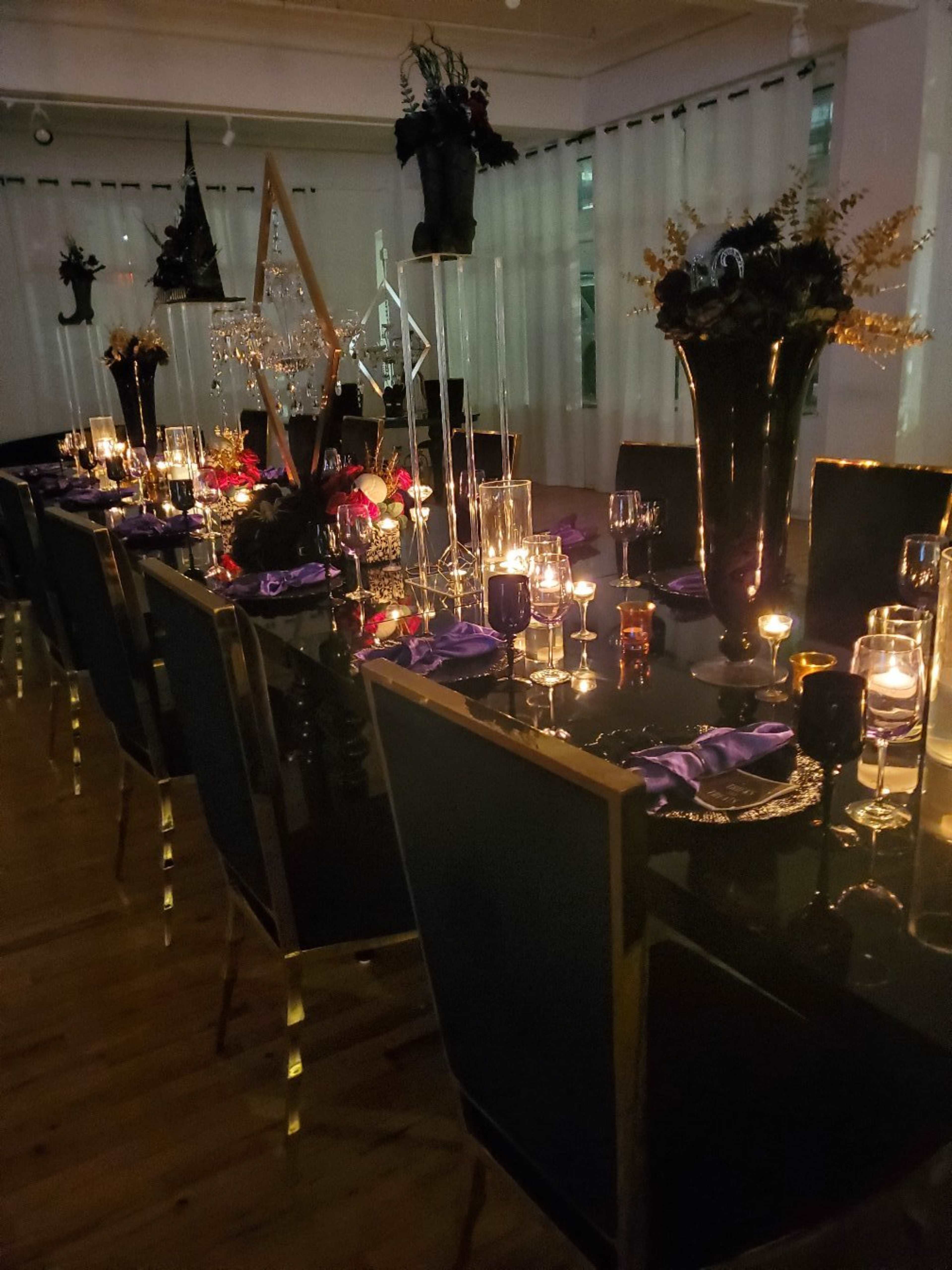 A long, elegantly set dining table is illuminated by candles and decorated with dark floral arrangements and glassware.
