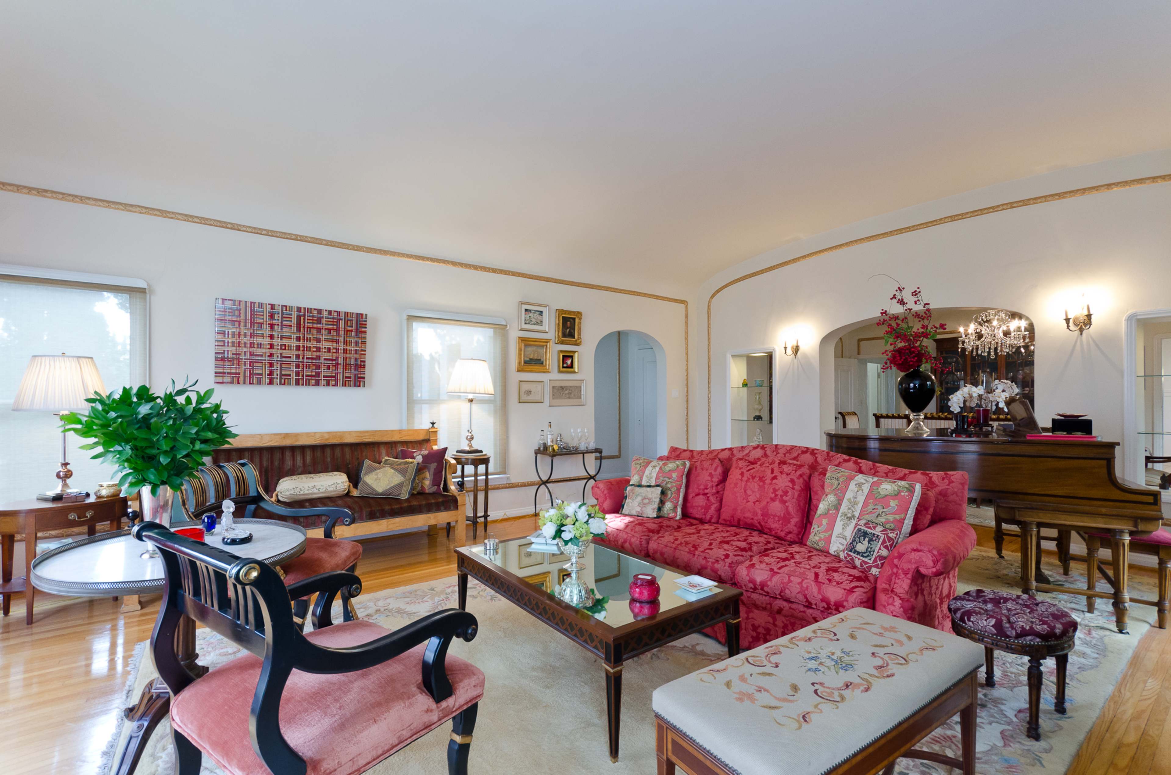 A spacious living room featuring a pink floral sofa, a wooden piano, and various decorative elements on the walls.
