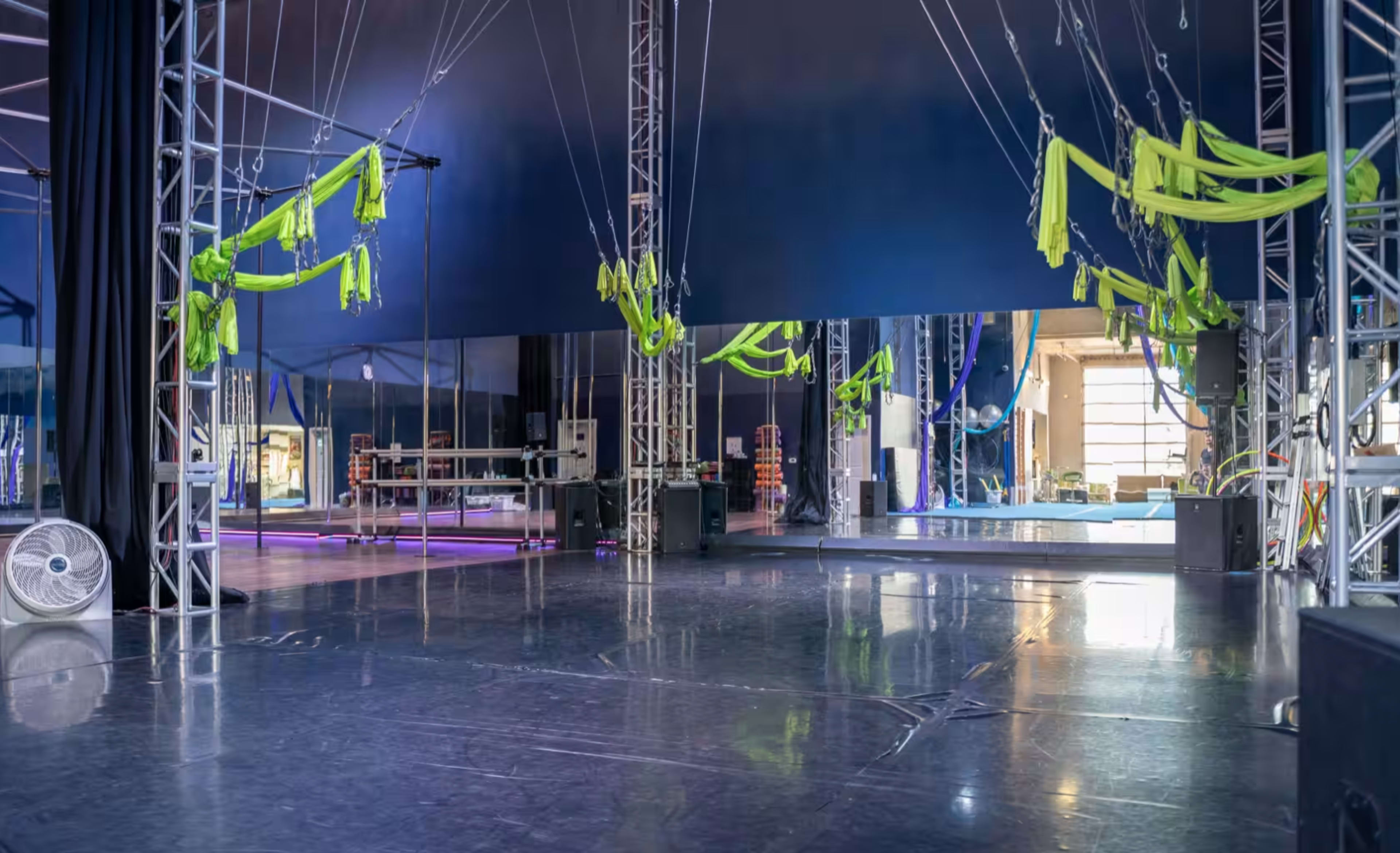 A spacious studio with a polished floor features hanging green fabric and large mirrors along one wall.