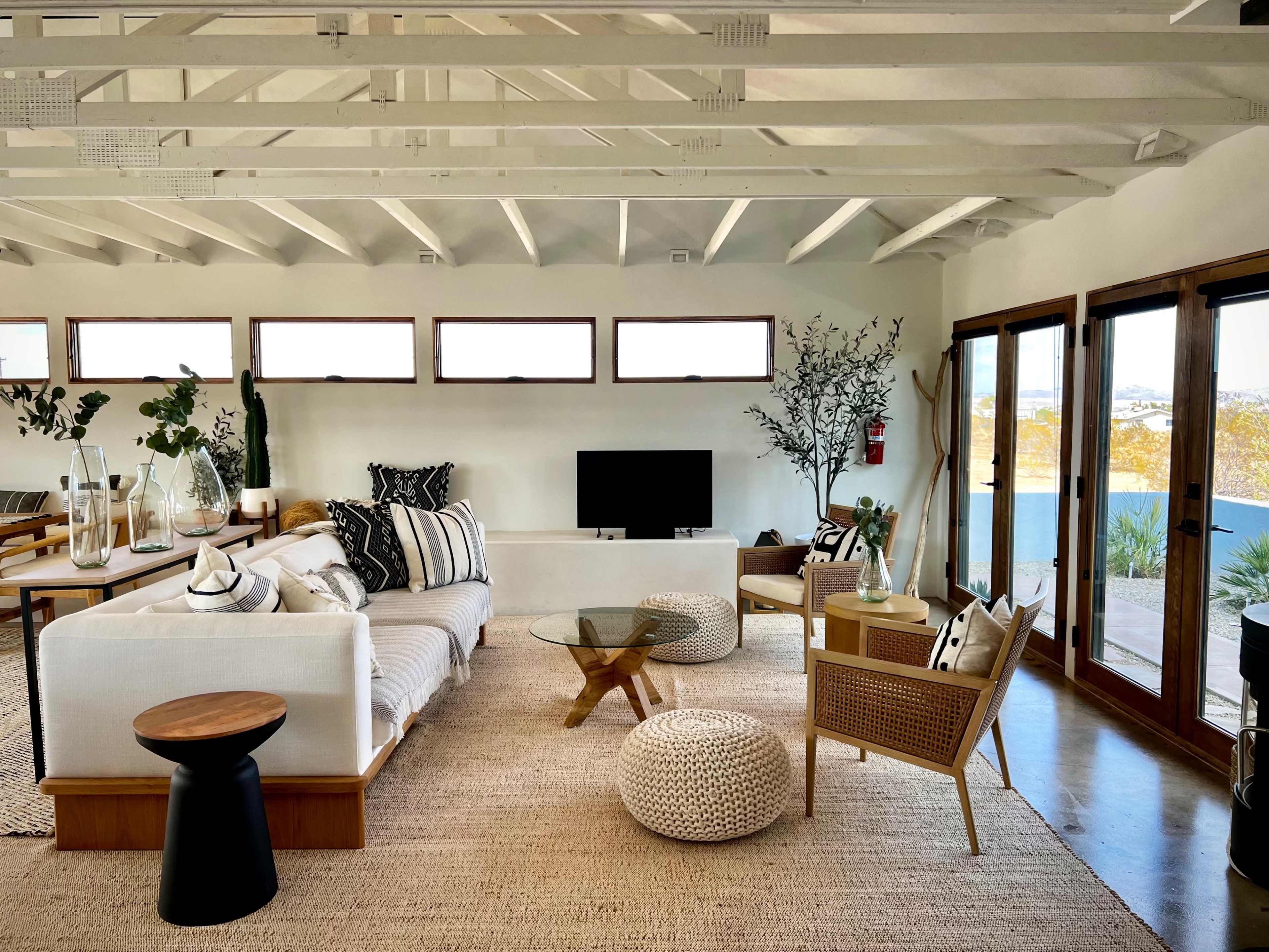 The image shows a spacious, modern living room with a white sofa, a wooden coffee table, and large windows that overlook a scenic view.