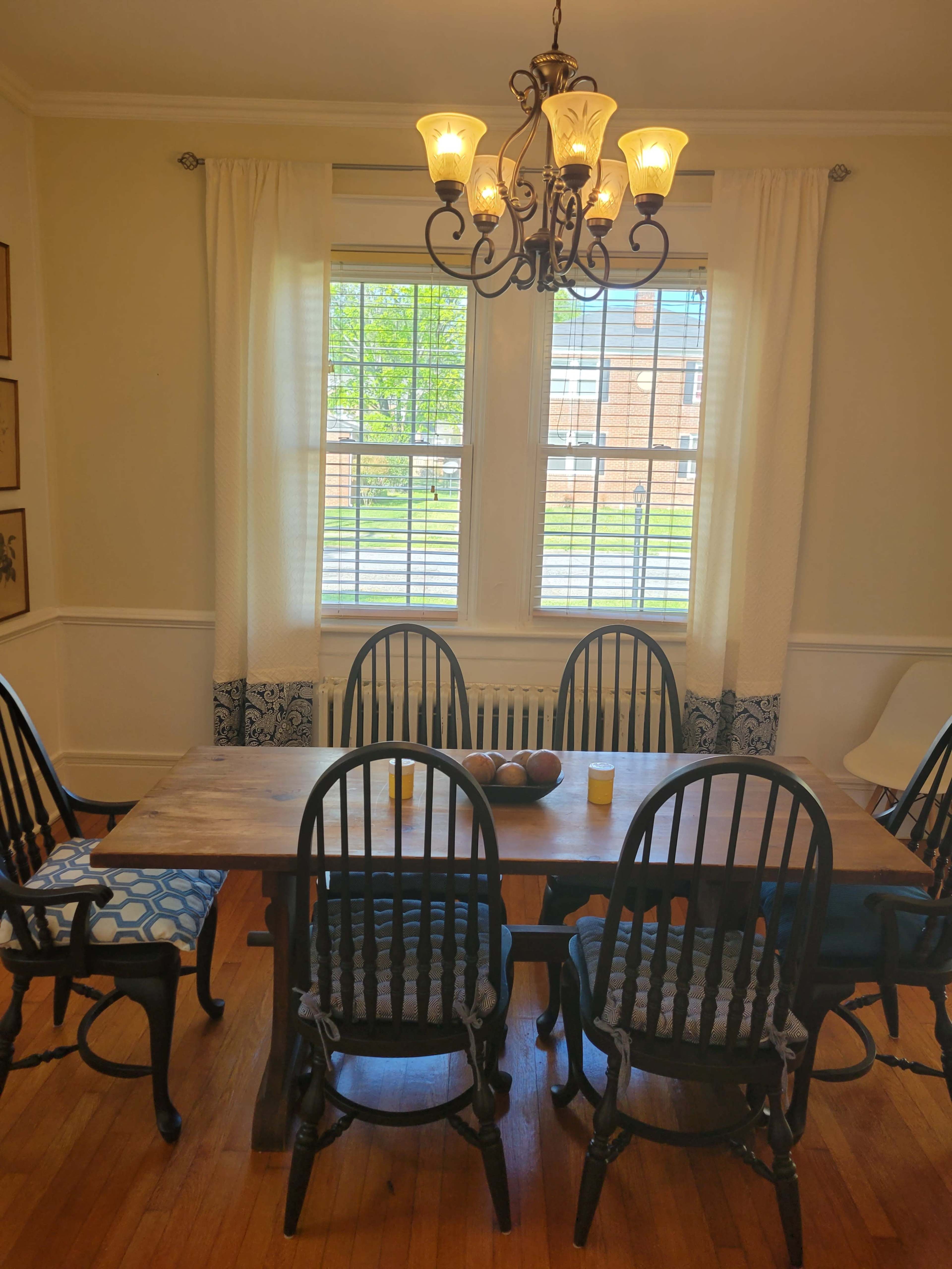A dining room with a large wooden table surrounded by six black wooden chairs and a decorative chandelier above.