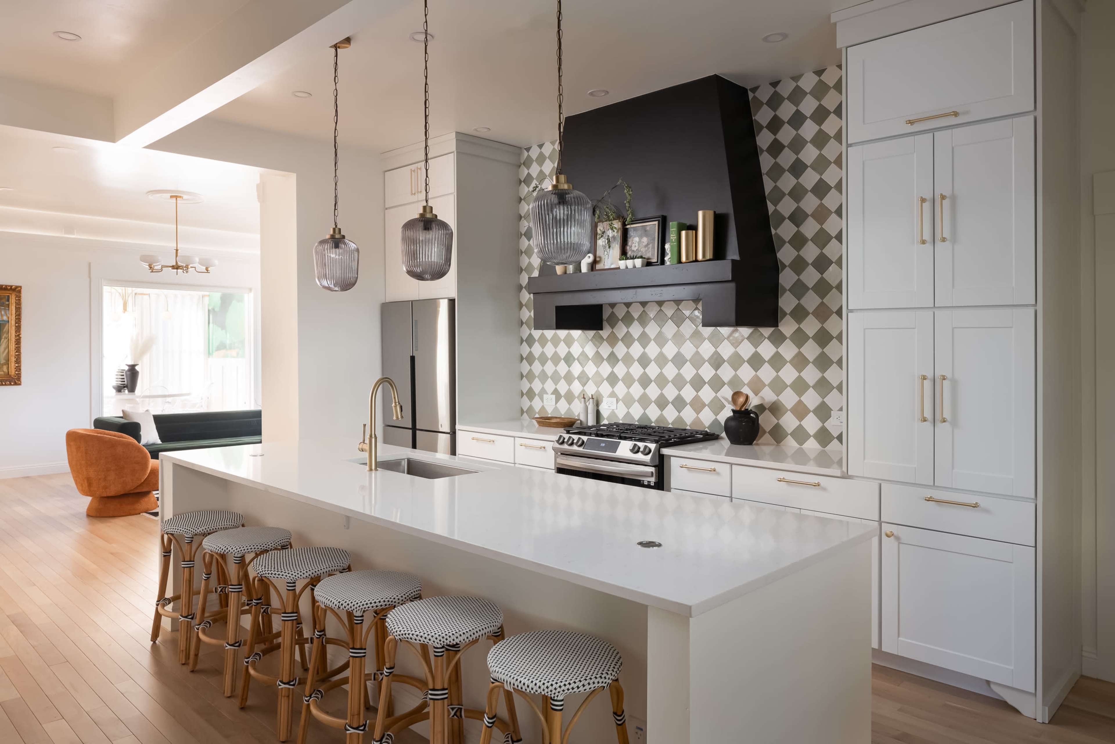 A modern kitchen features a large island with bar stools, stylish pendant lighting, and a patterned backsplash behind the stove.