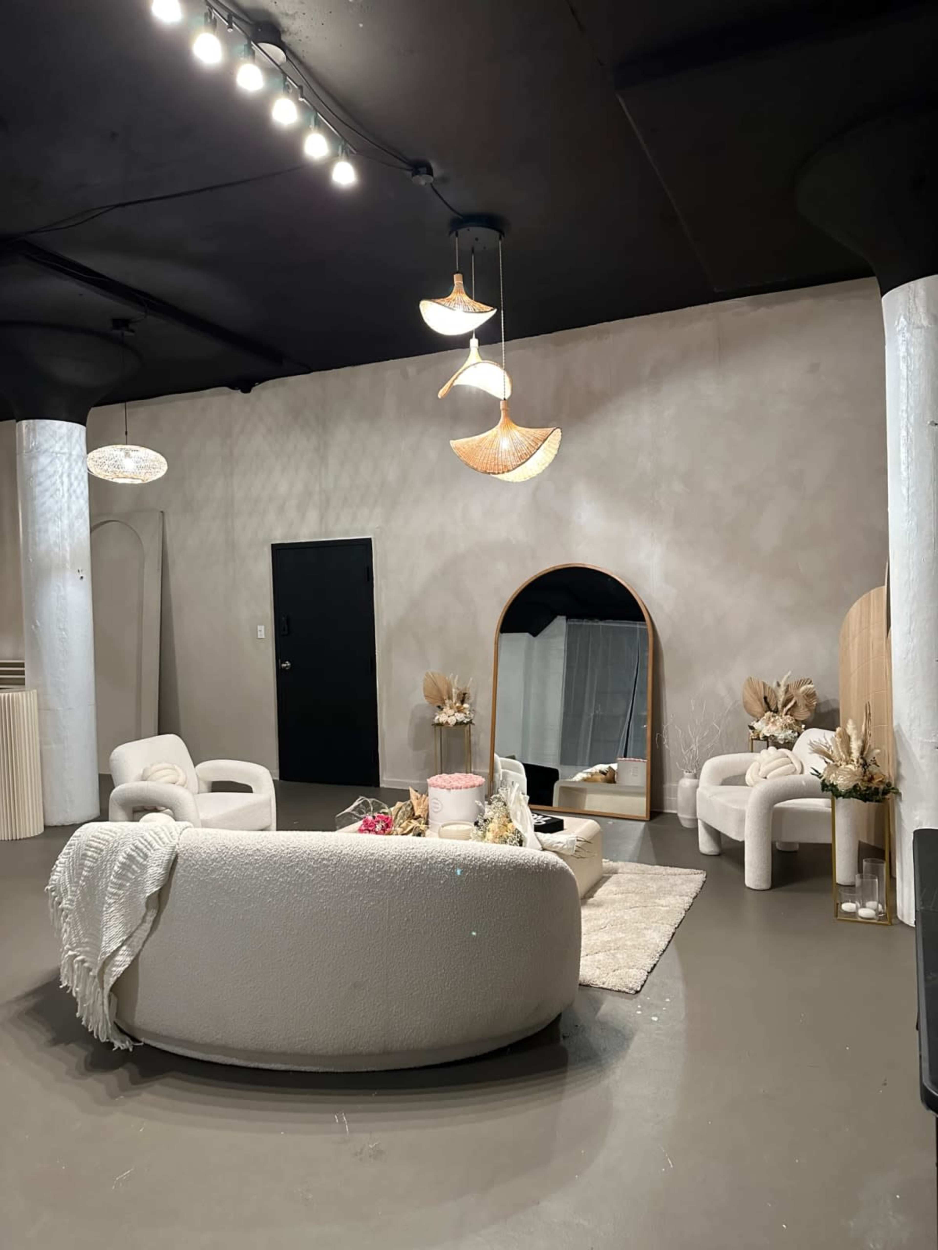 The image features a modern, minimalist living space with a curved sofa, two armchairs, a coffee table, and decorative elements, all set against a neutral-colored wall and ceiling.