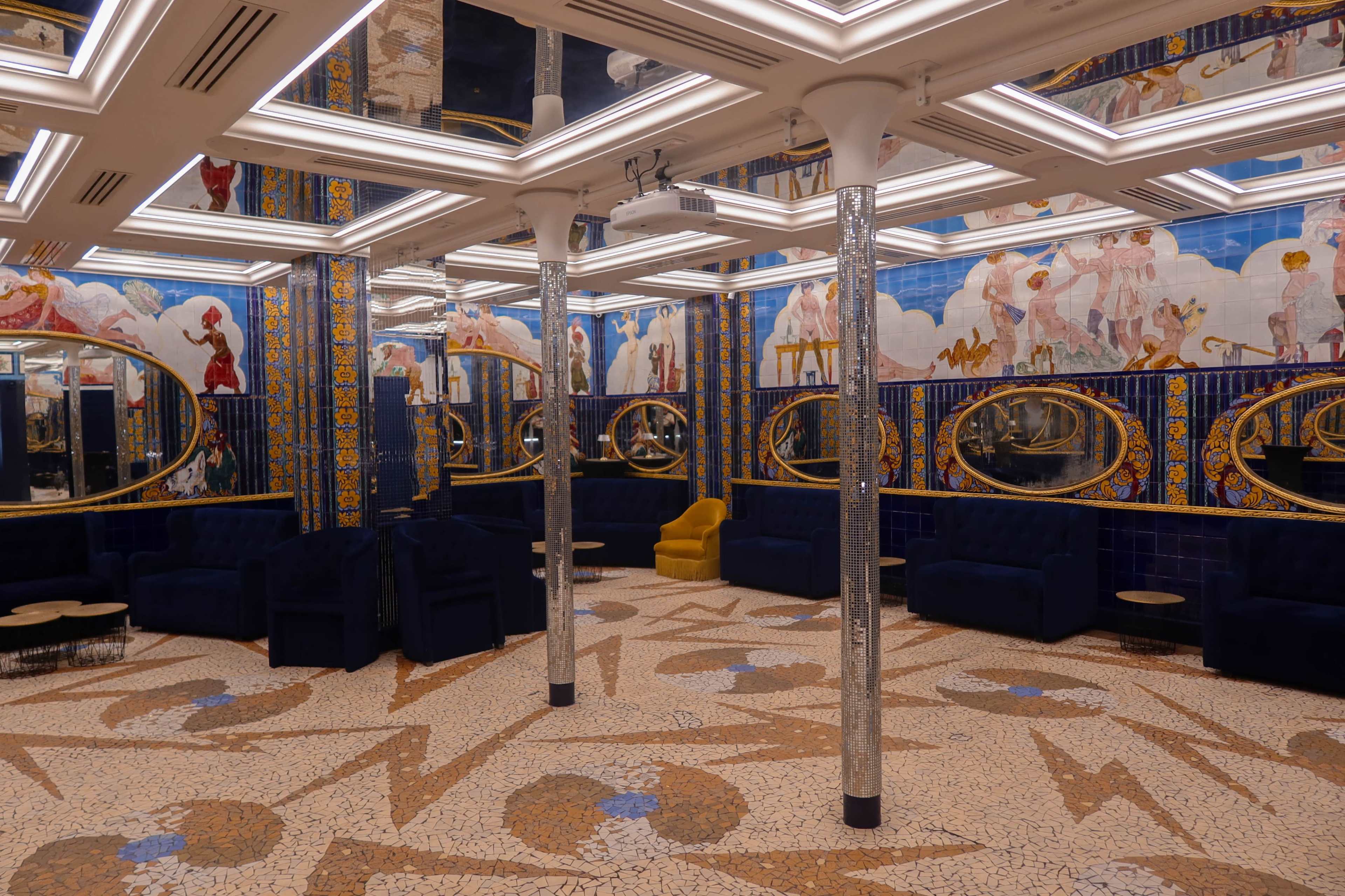 The interior features a decorative room with mirrored walls, blue seating, and a patterned tile floor.