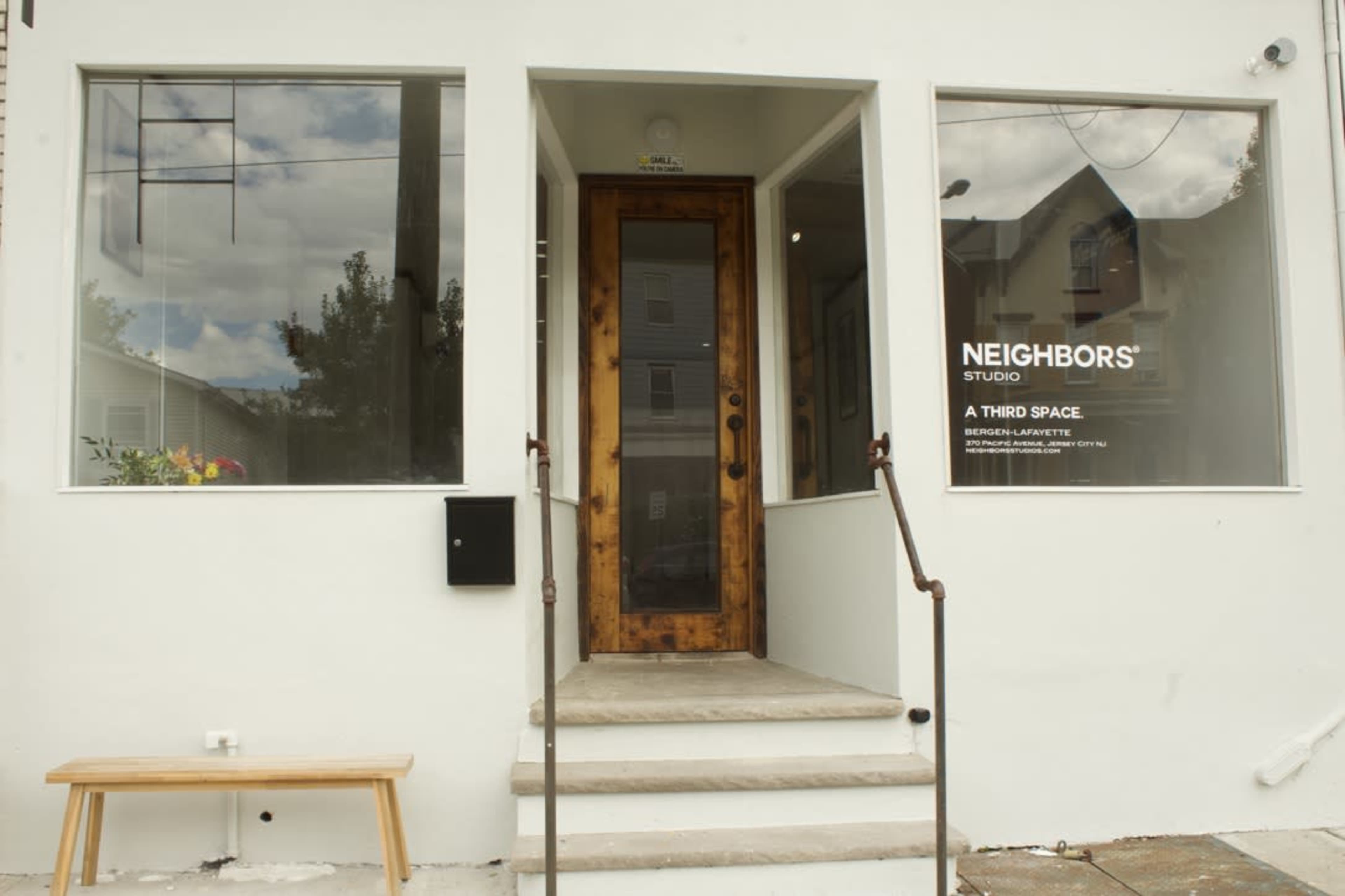 The image shows the entrance of a studio named "Neighbors" with large windows and a wooden door, flanked by a small set of steps.