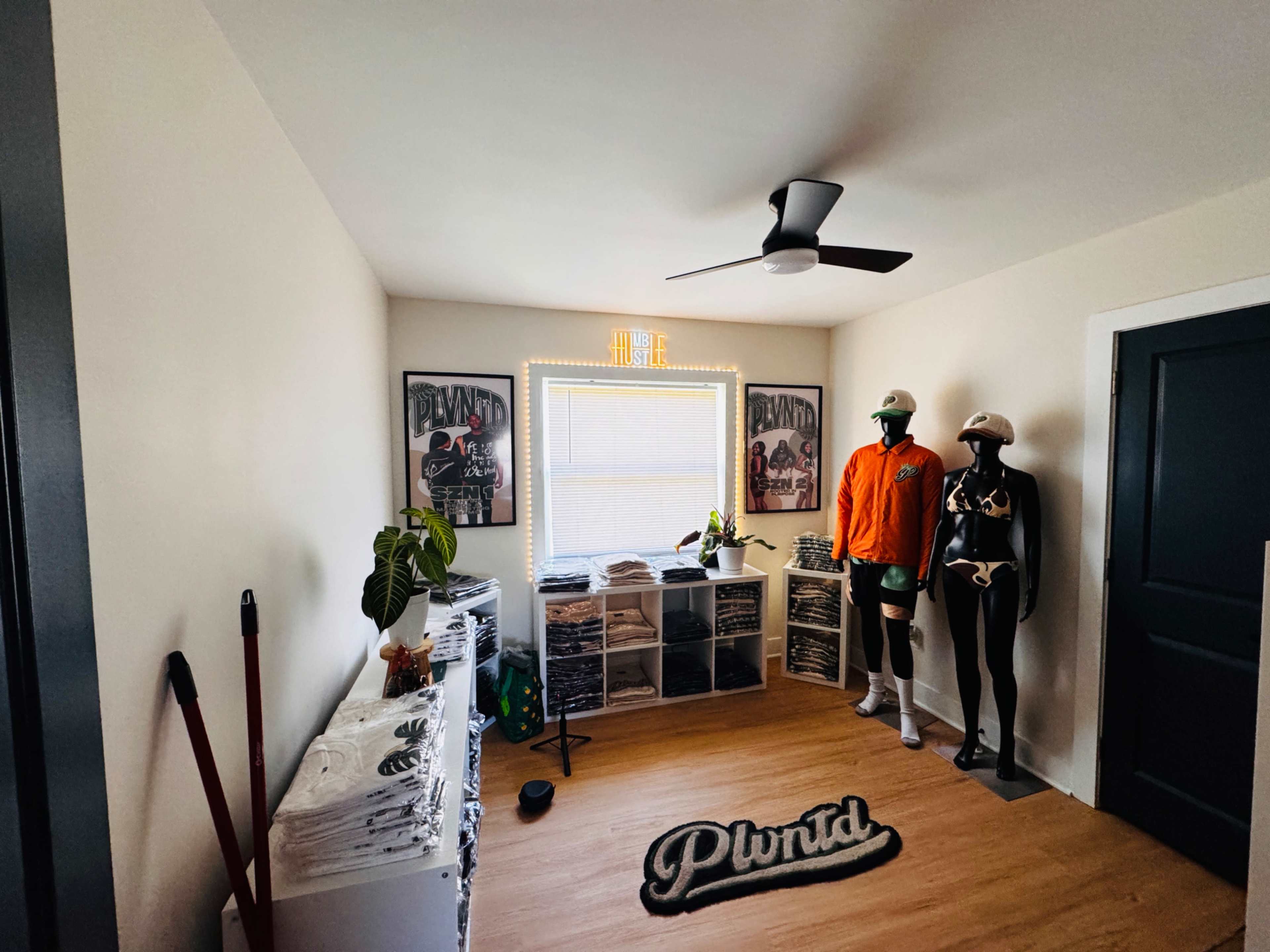 The room features two mannequins dressed in athletic attire, shelves filled with apparel, a ceiling fan, and framed posters on the walls.