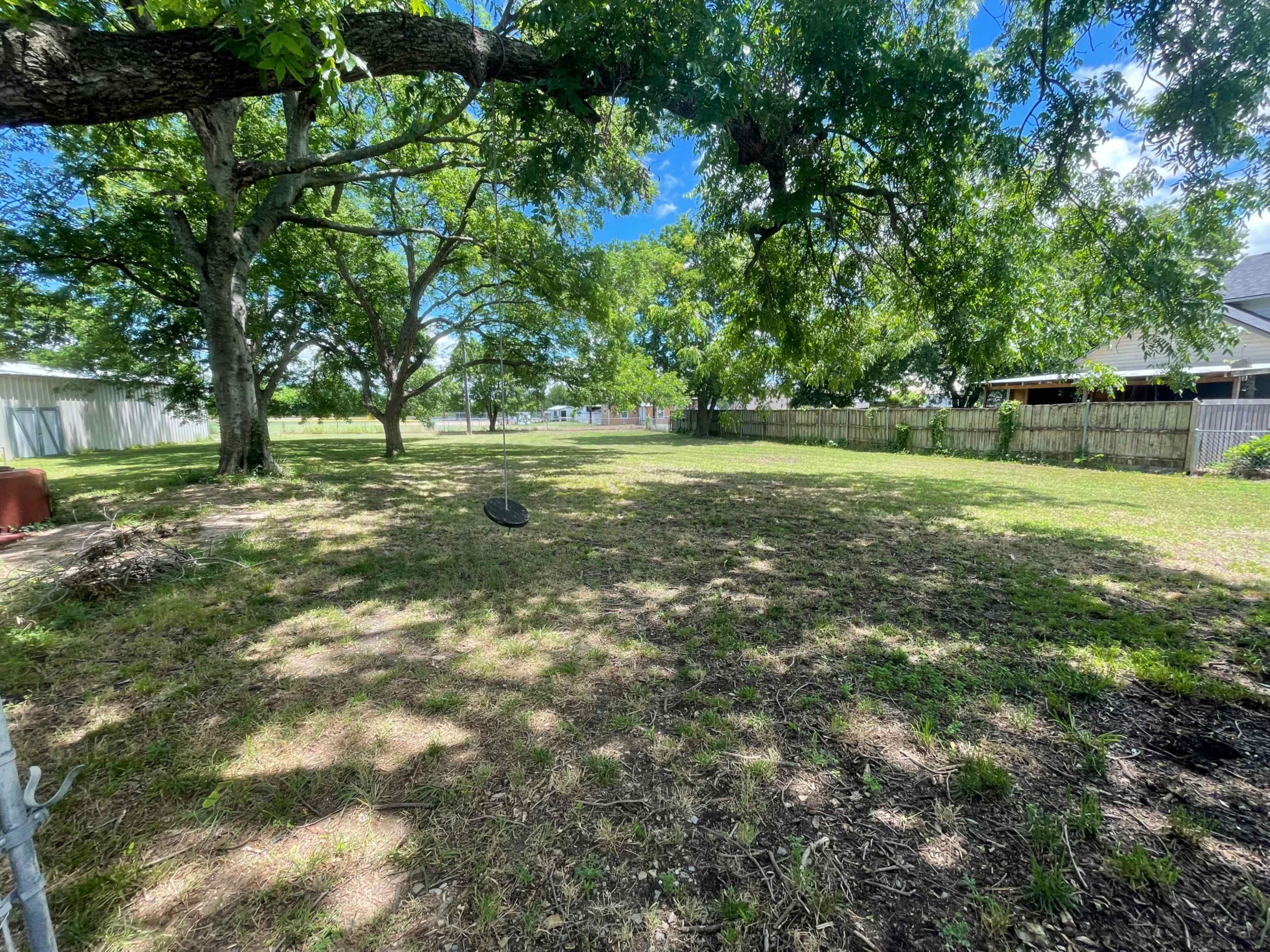 The image shows a spacious backyard with grass and scattered trees, featuring a swing hanging from a tree branch.