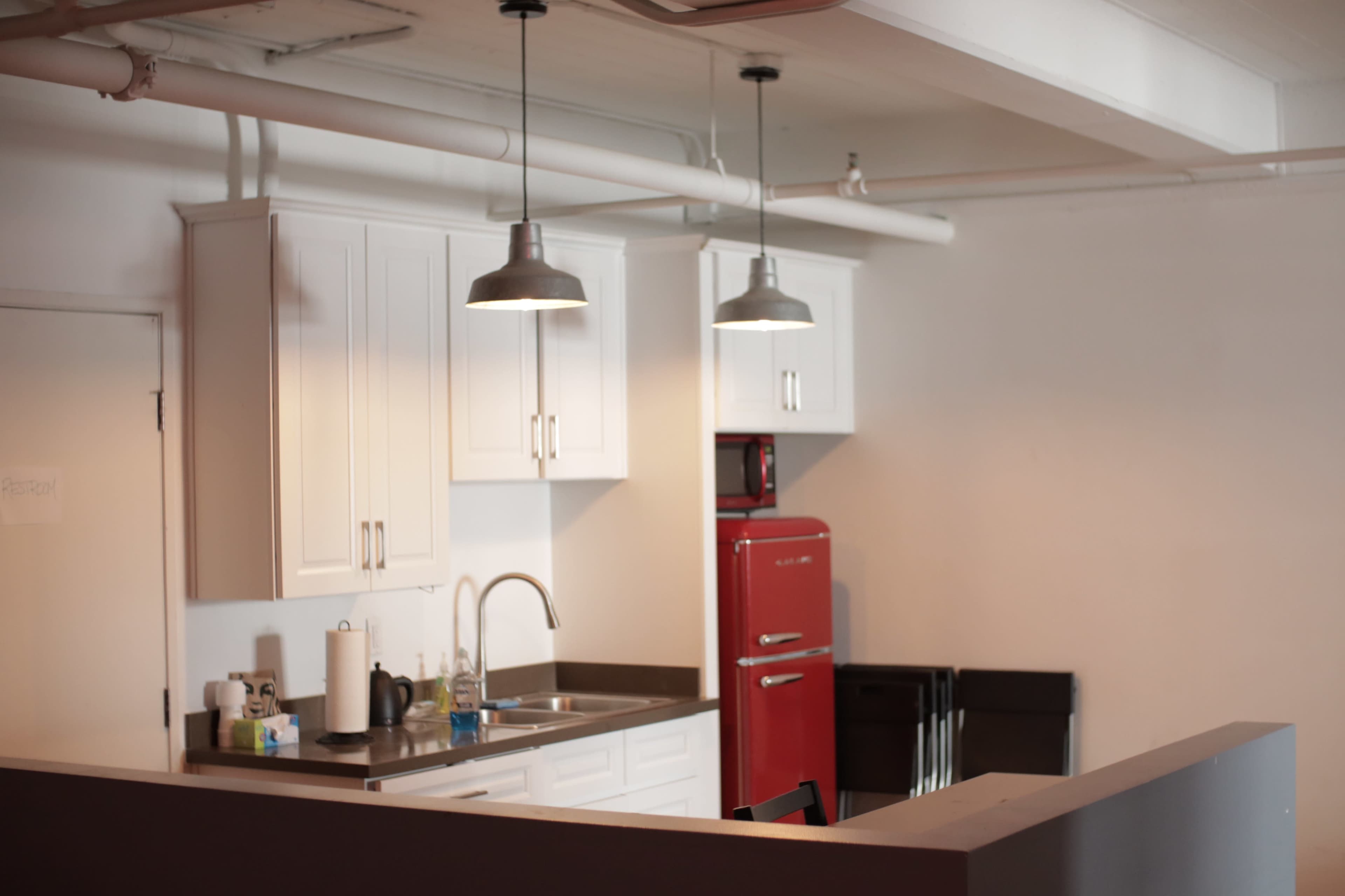 A modern kitchen featuring white cabinets, a red refrigerator, and metallic pendant lights hanging above the countertop.