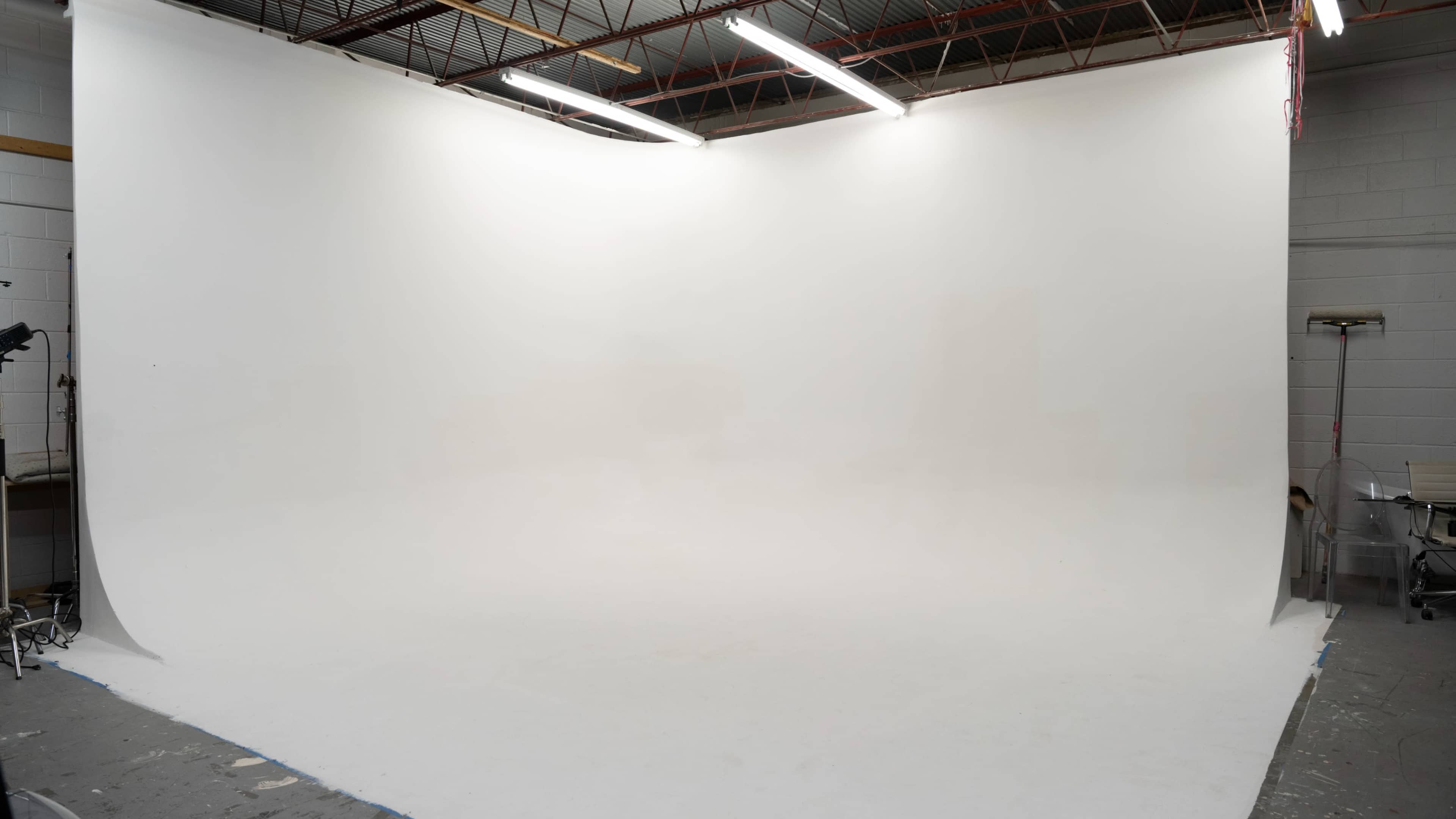 An empty photography studio with a seamless white backdrop and overhead lighting.