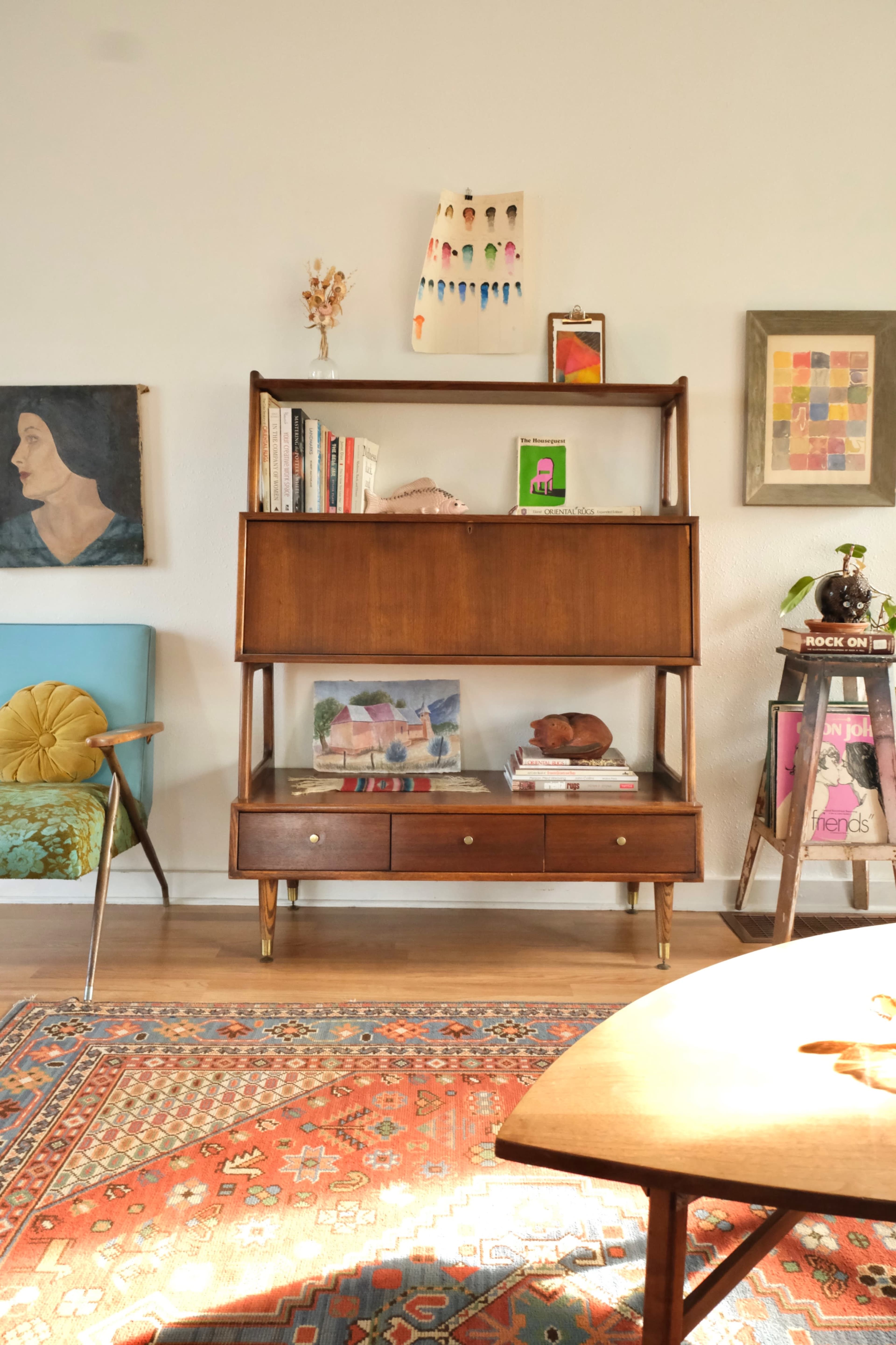 A mid-century modern living room featuring a wooden shelving unit, colorful artworks, and a patterned area rug.