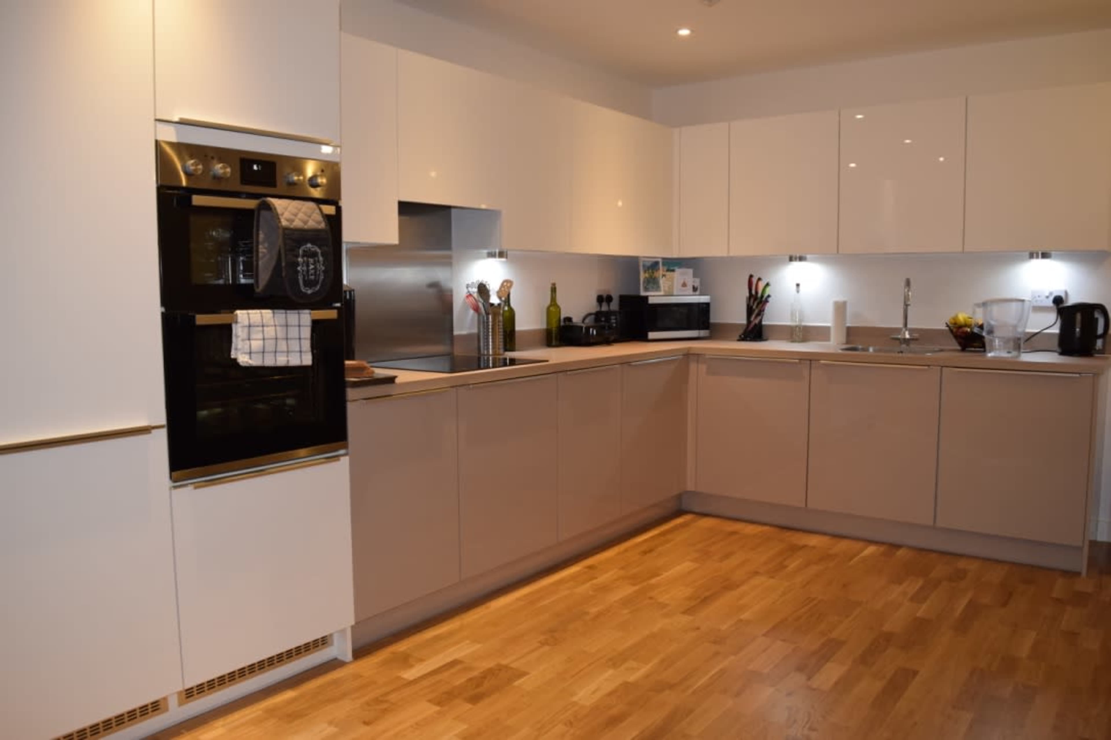A modern kitchen with light-colored cabinetry, stainless steel appliances, and a wooden floor.