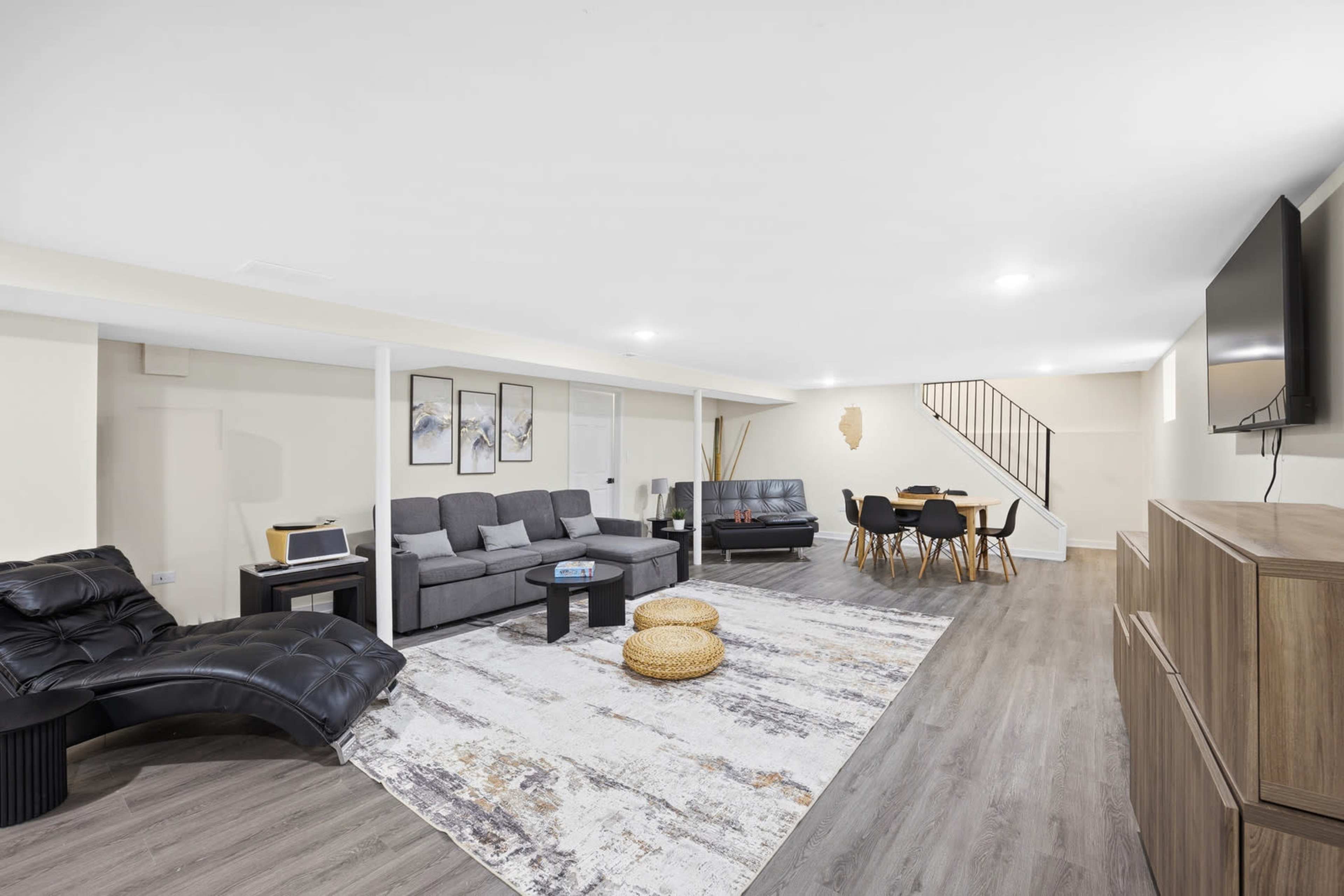 The image shows a spacious basement living area with two sofas, a dining table, and a television mounted on the wall.