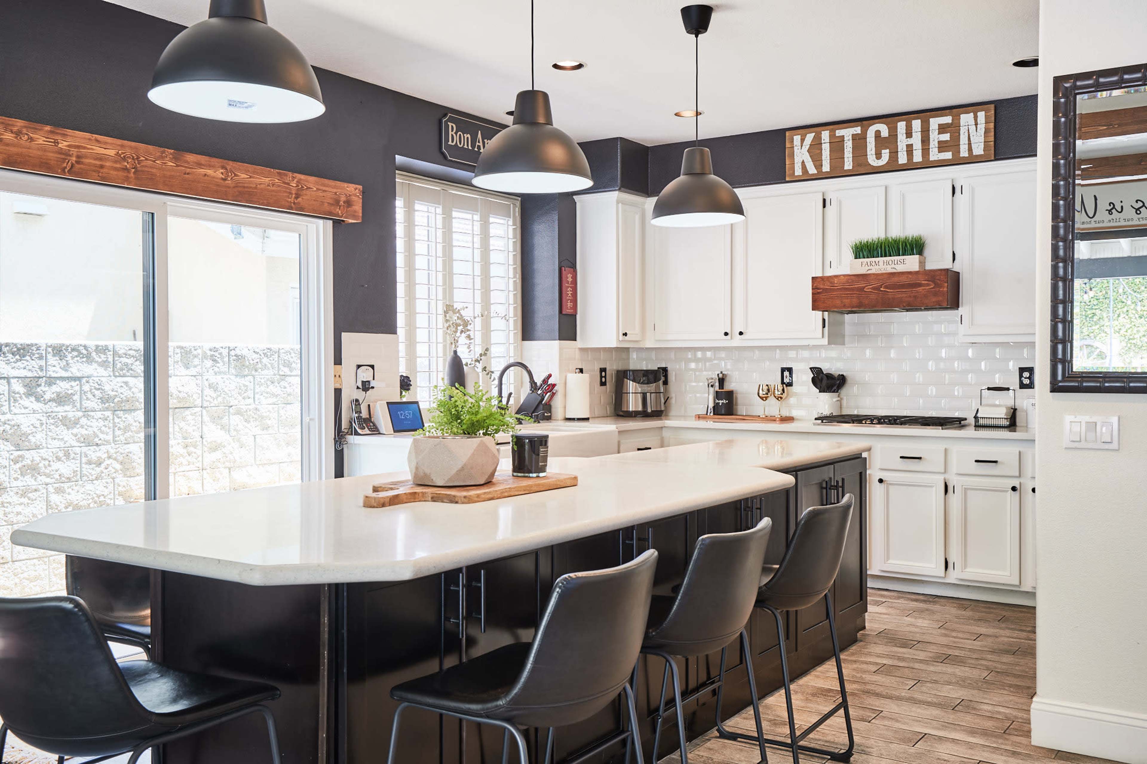 A modern kitchen with white cabinets, dark countertops, and bar seating, illuminated by pendant lights.