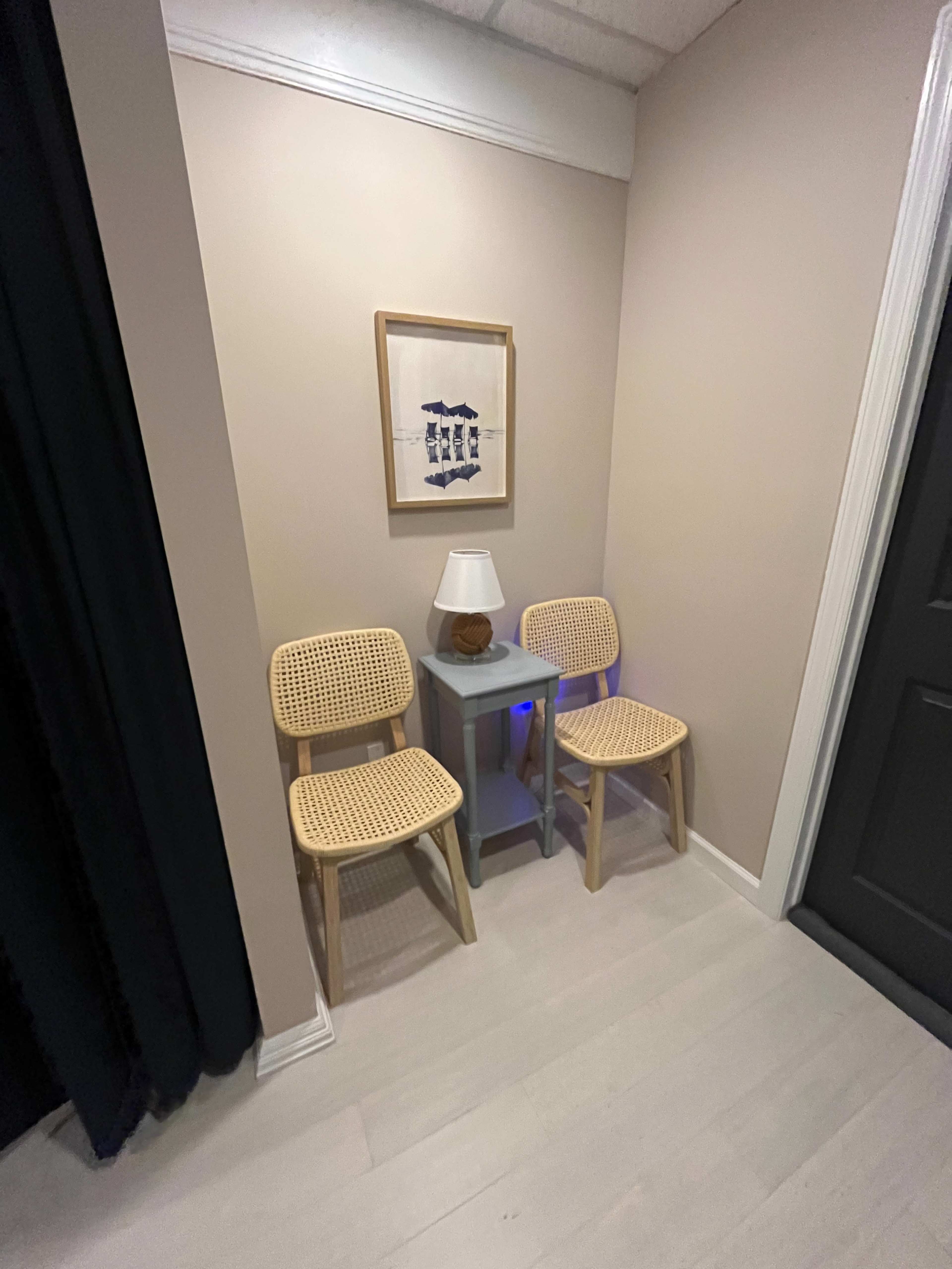 A small corner features two woven chairs next to a side table with a lamp and a framed picture on the wall.