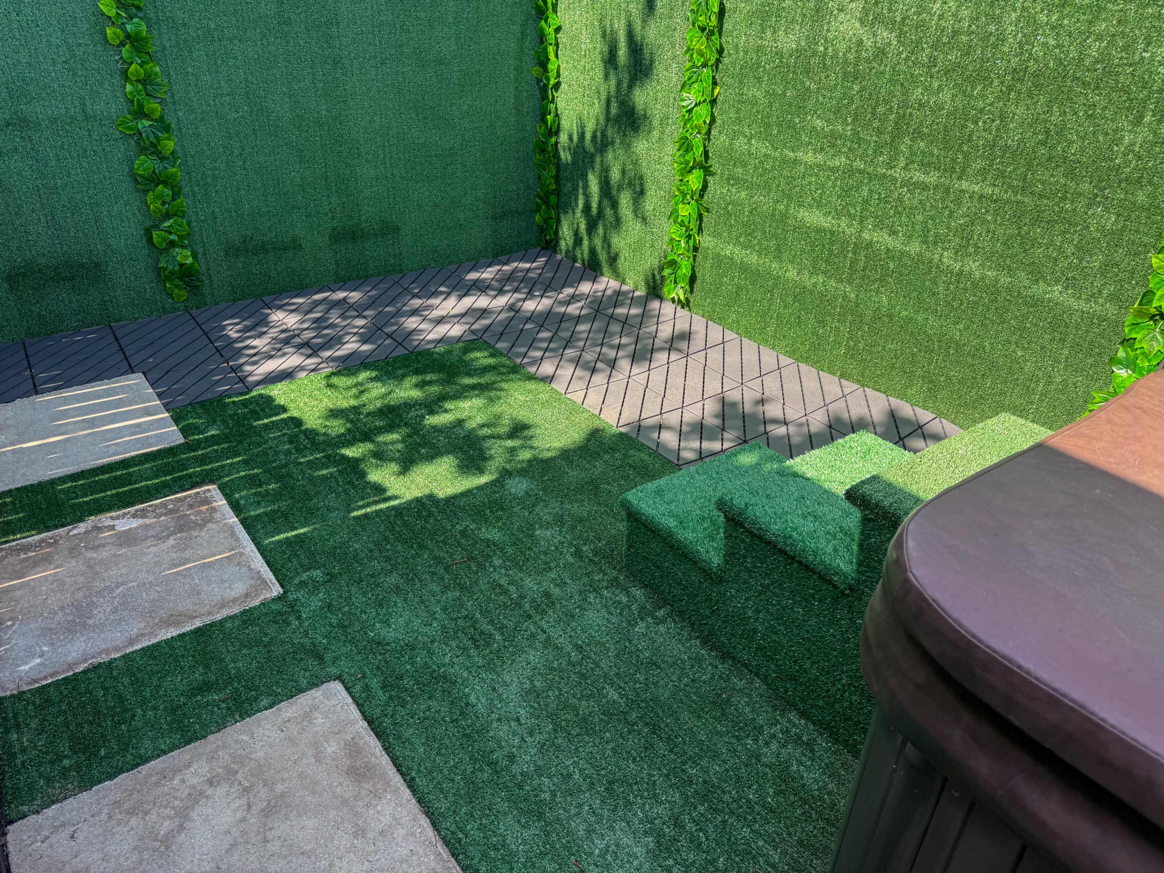 The image shows a landscaped outdoor area with artificial grass, stone slabs, and a small set of stairs leading to a raised section.