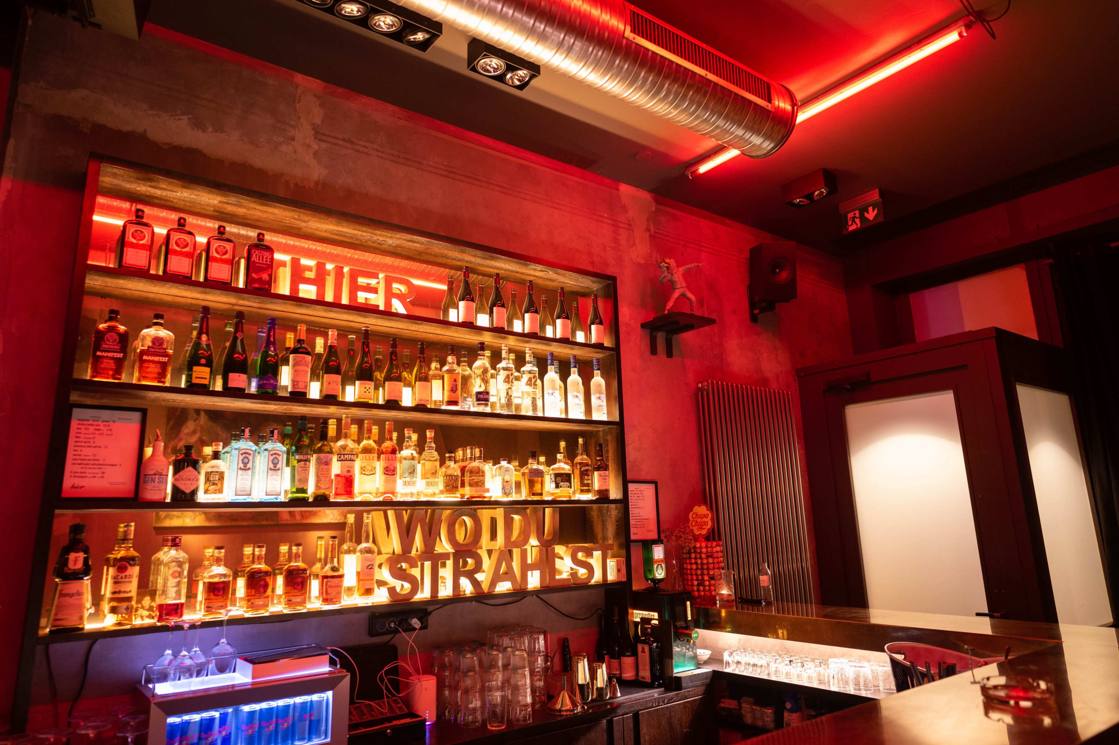 The image shows a bar with various bottles of liquor arranged on a shelf, illuminated by red LED lighting.