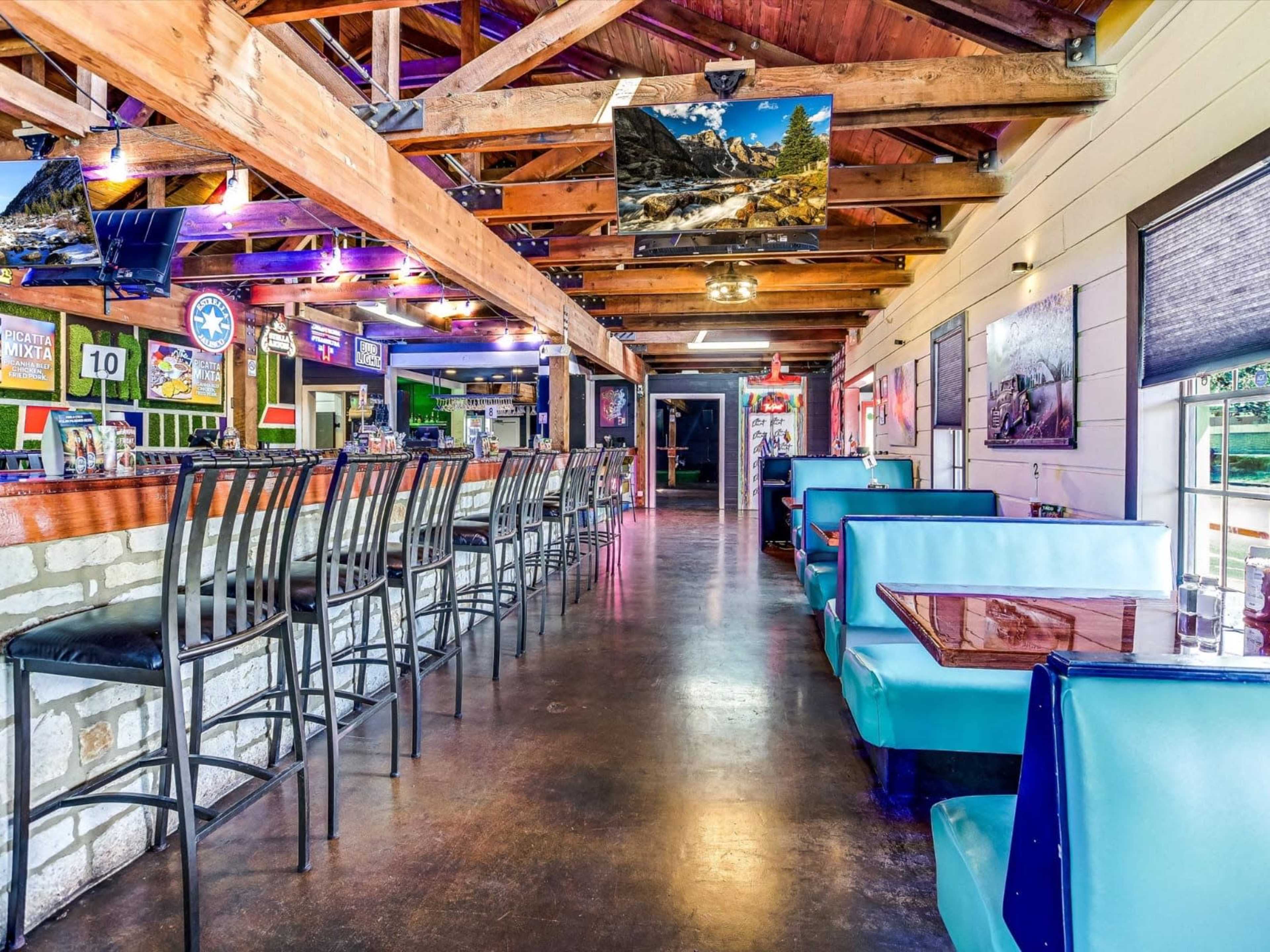 The image shows the interior of a restaurant or bar featuring a long bar area with high stools and blue booths along the sides.