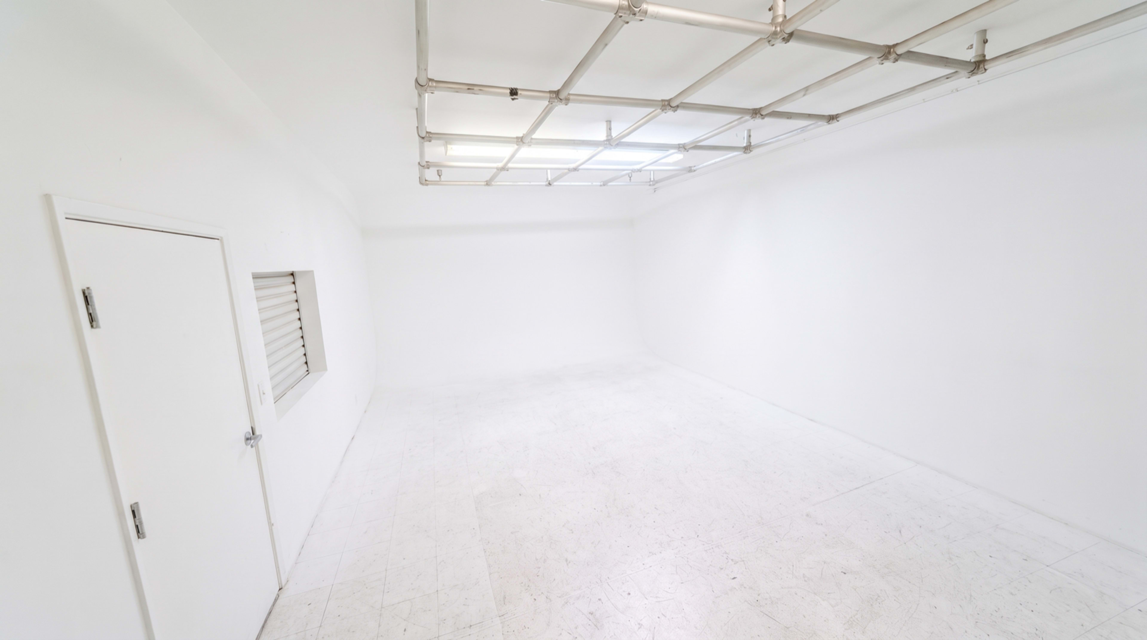 The image depicts a spacious, empty room with white walls, a white floor, and a ceiling with a translucent section.