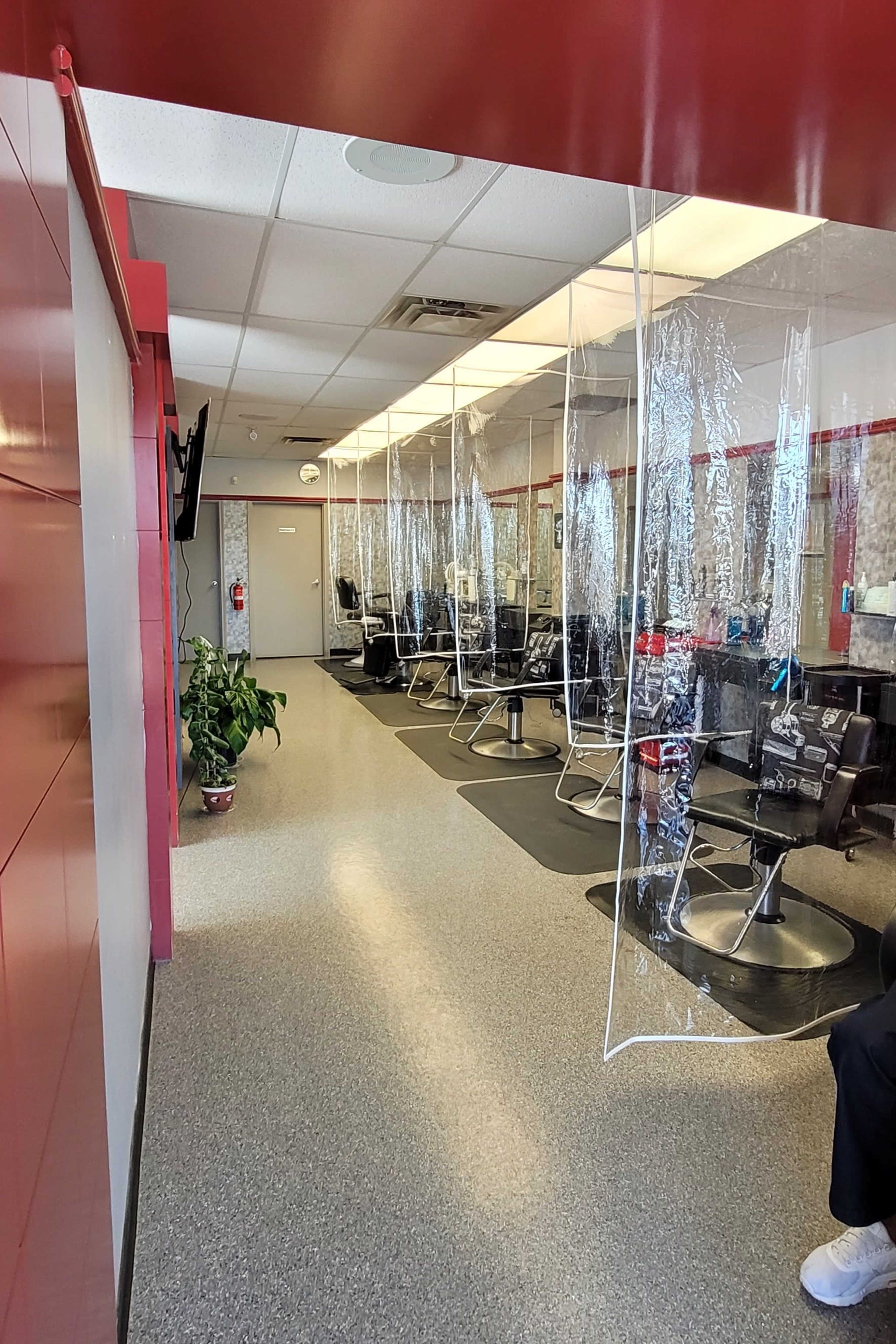 A salon interior with several styling chairs separated by clear plastic partitions along a long hallway.