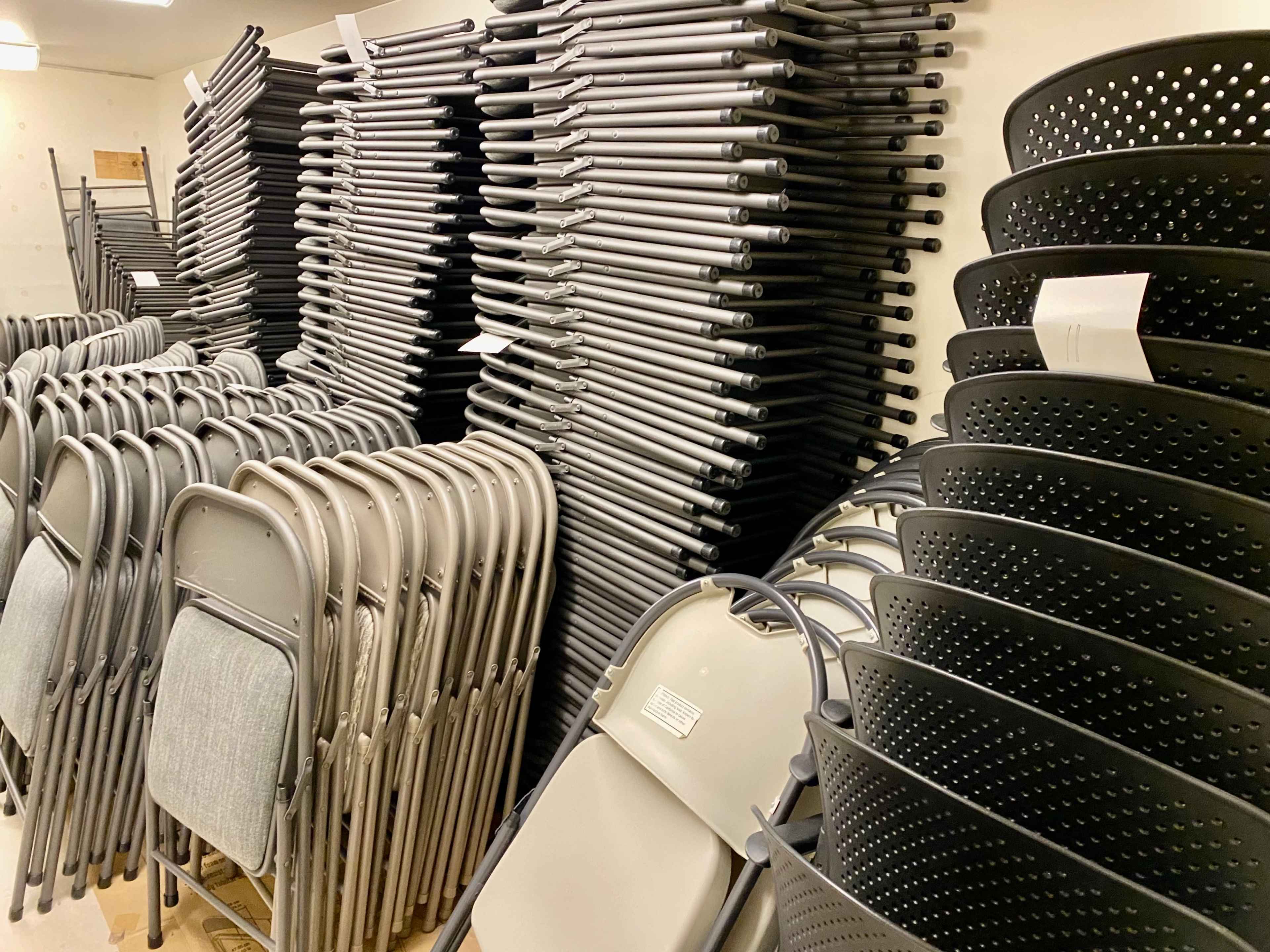 A storage room filled with neatly stacked folding chairs and black storage bins.