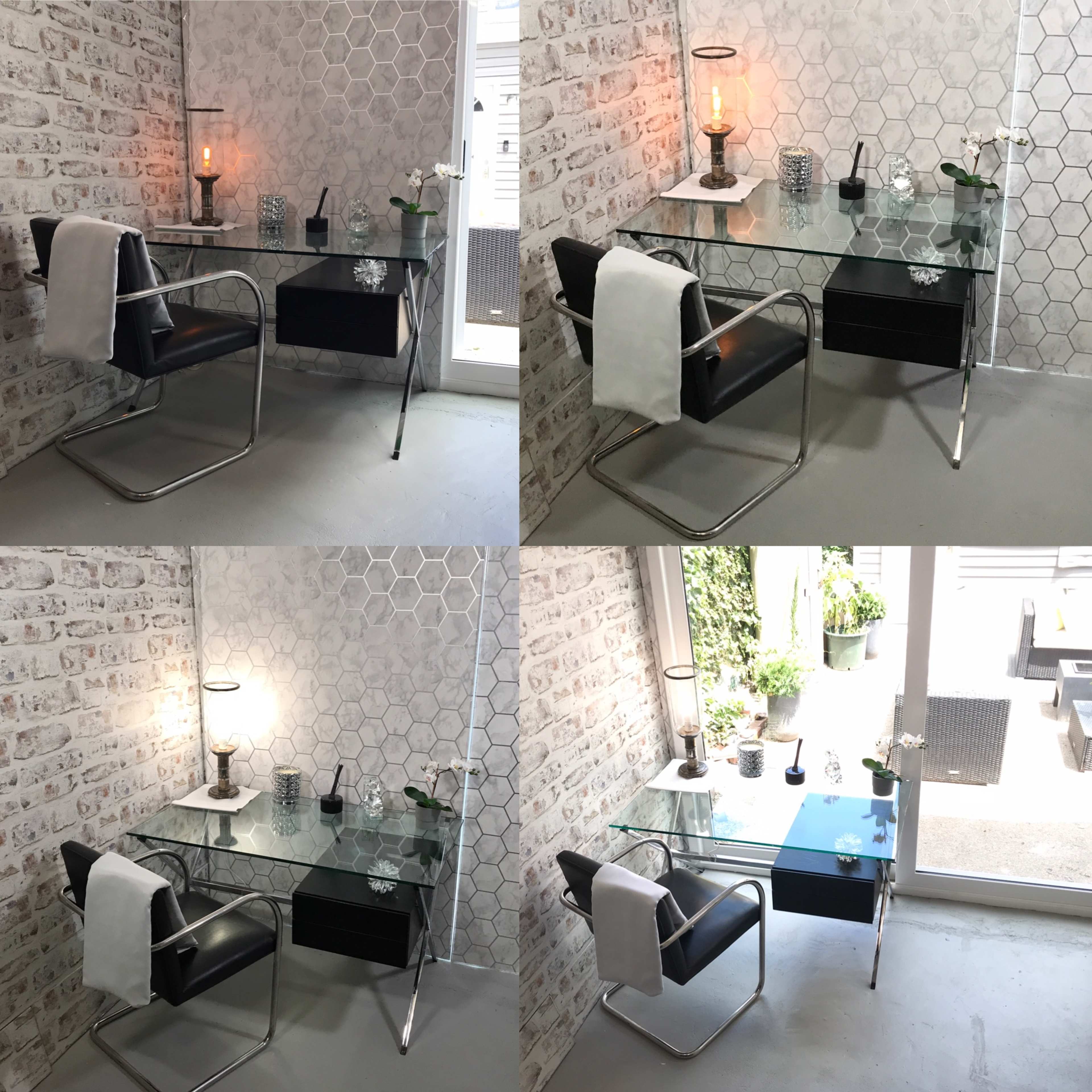 A modern glass desk with a black chair, a table lamp, and decorative items against a light brick wall.