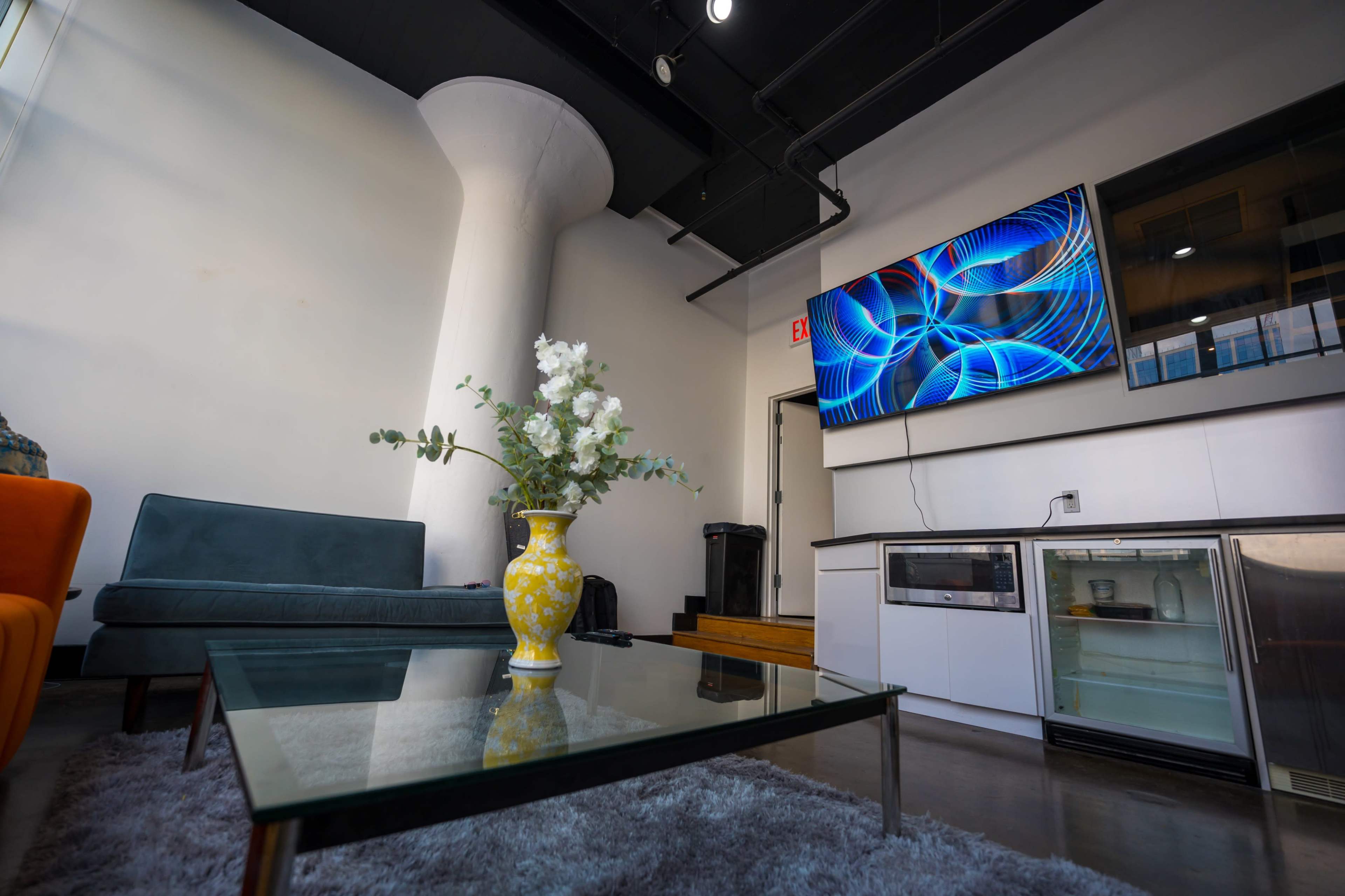A modern living space featuring a green sofa, a glass coffee table with a vase of flowers, and a wall-mounted television.