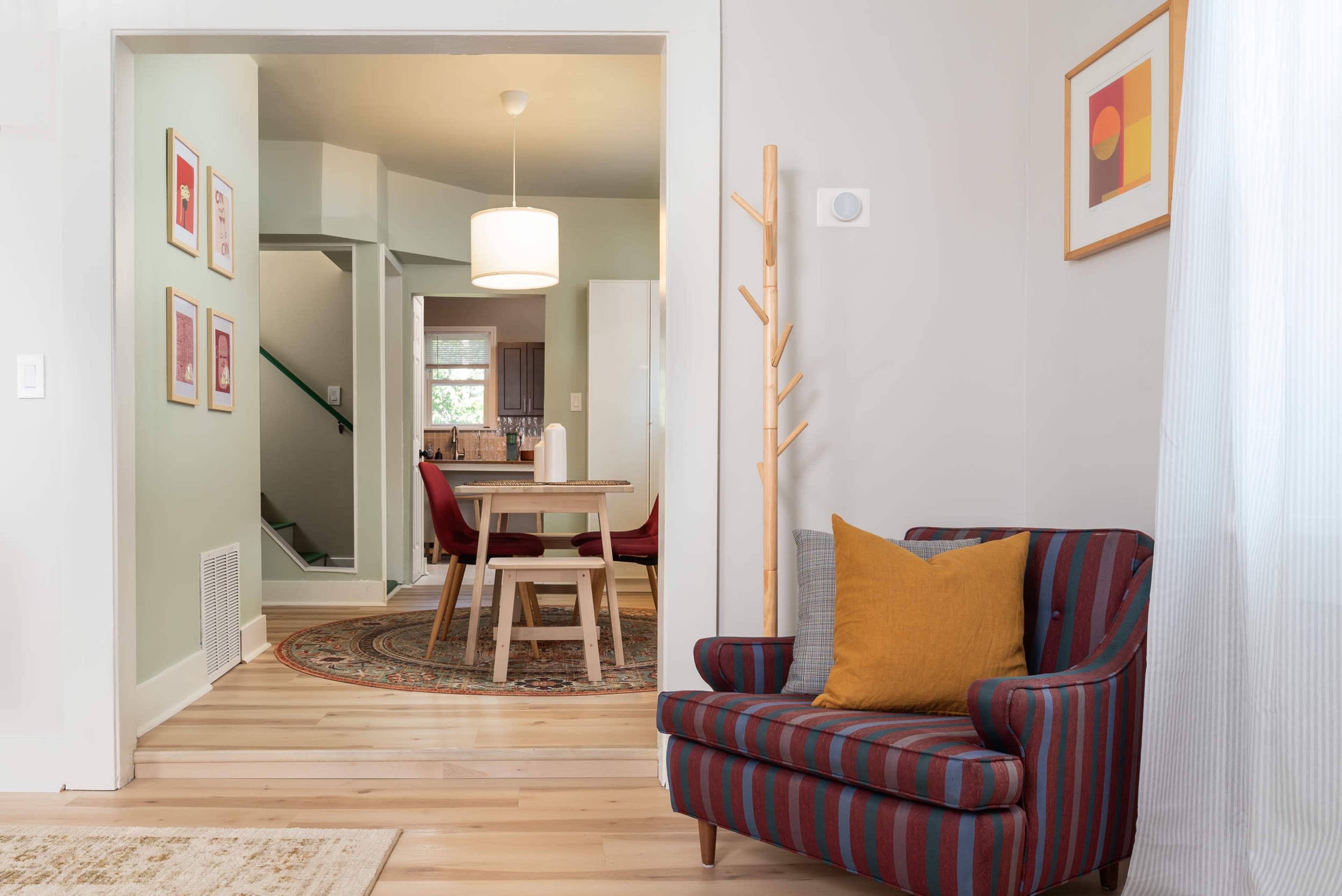 A striped armchair with a yellow cushion sits in the foreground, leading to a dining area with a round table and red chairs in the background.