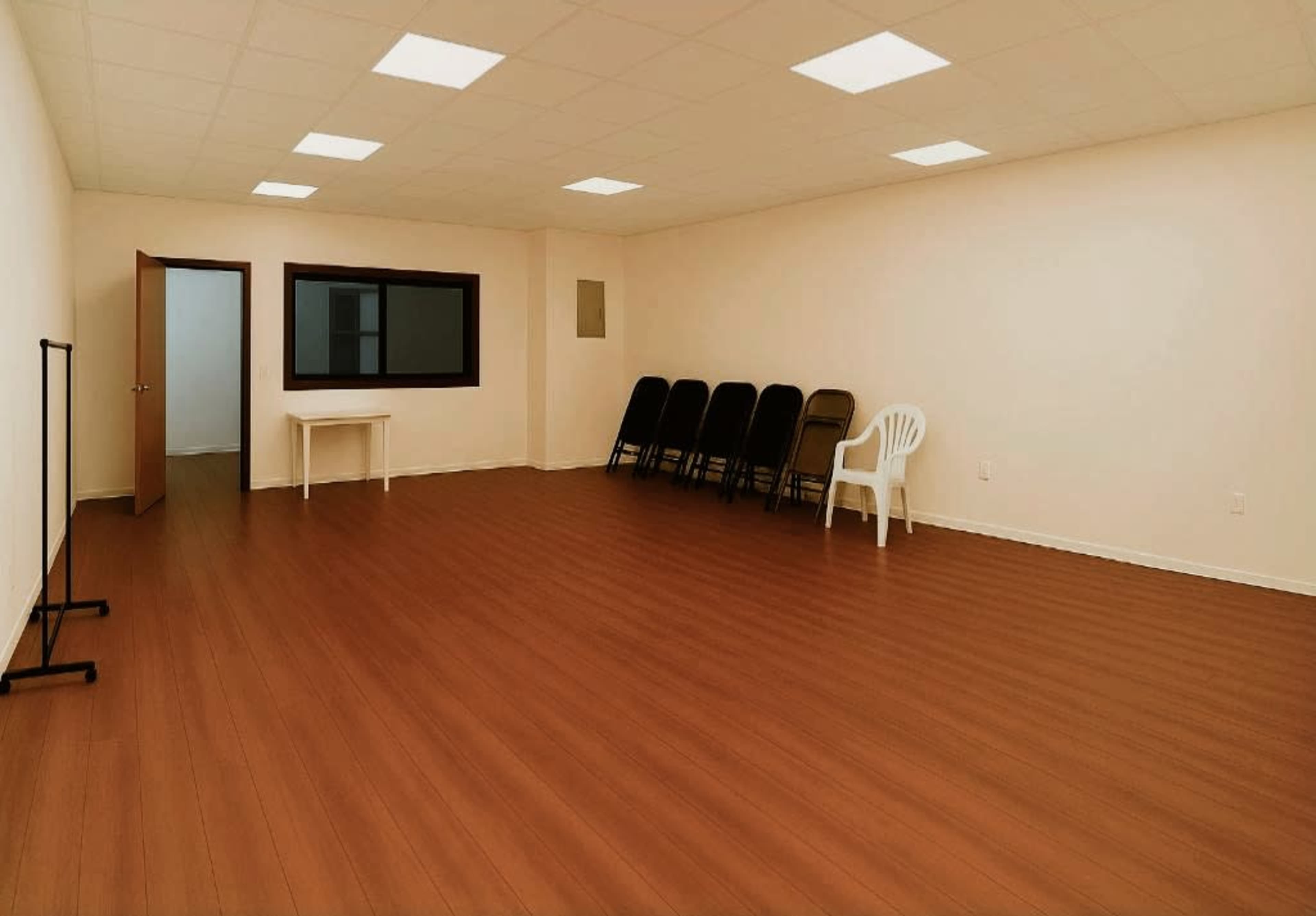 The interior of a vacant room features a smooth floor, a window, a table, and a row of folding chairs against one wall.