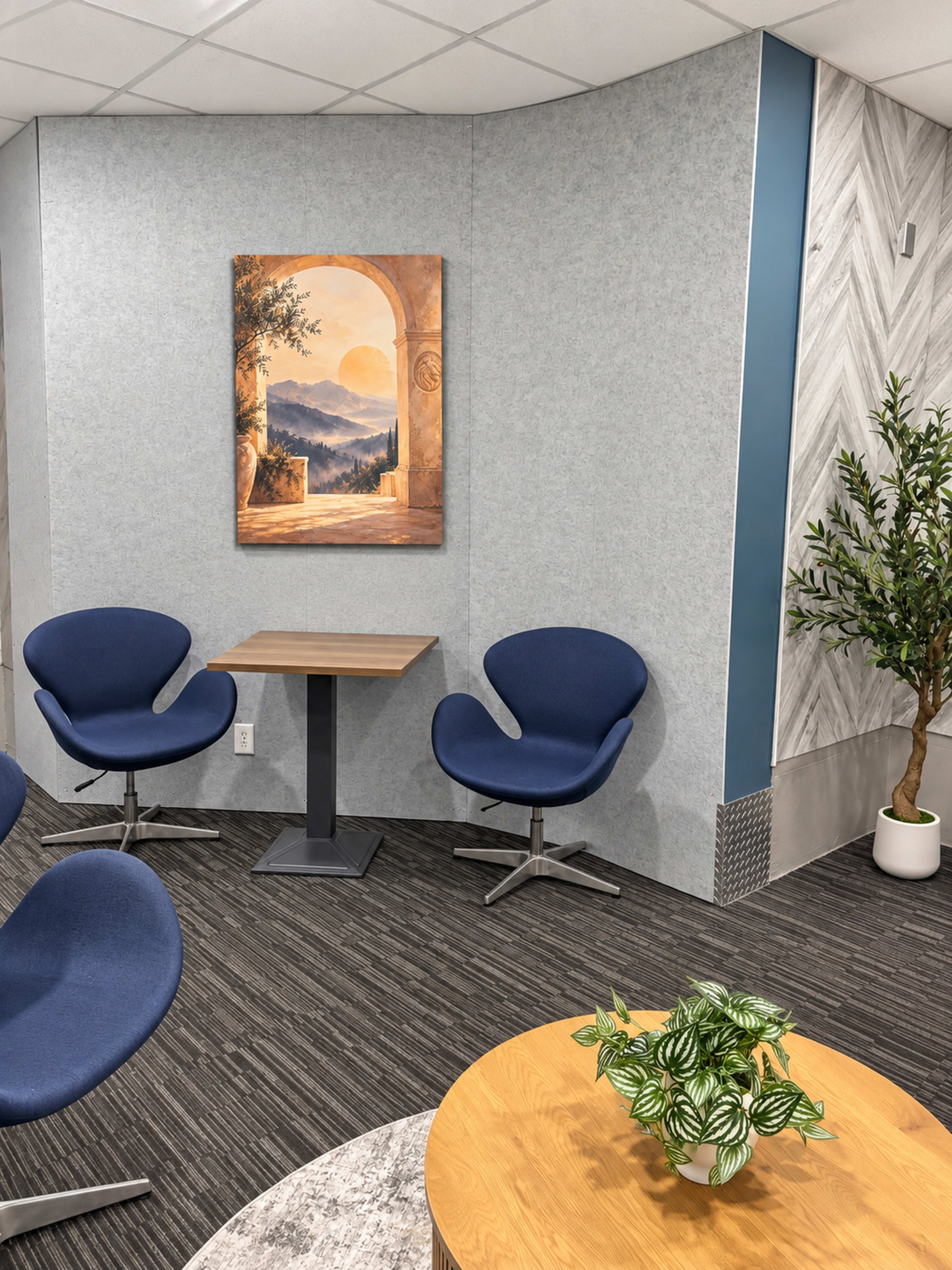 The image depicts a modern waiting area featuring two blue chairs, a small wooden table, a decorative painting on the wall, and a potted plant.