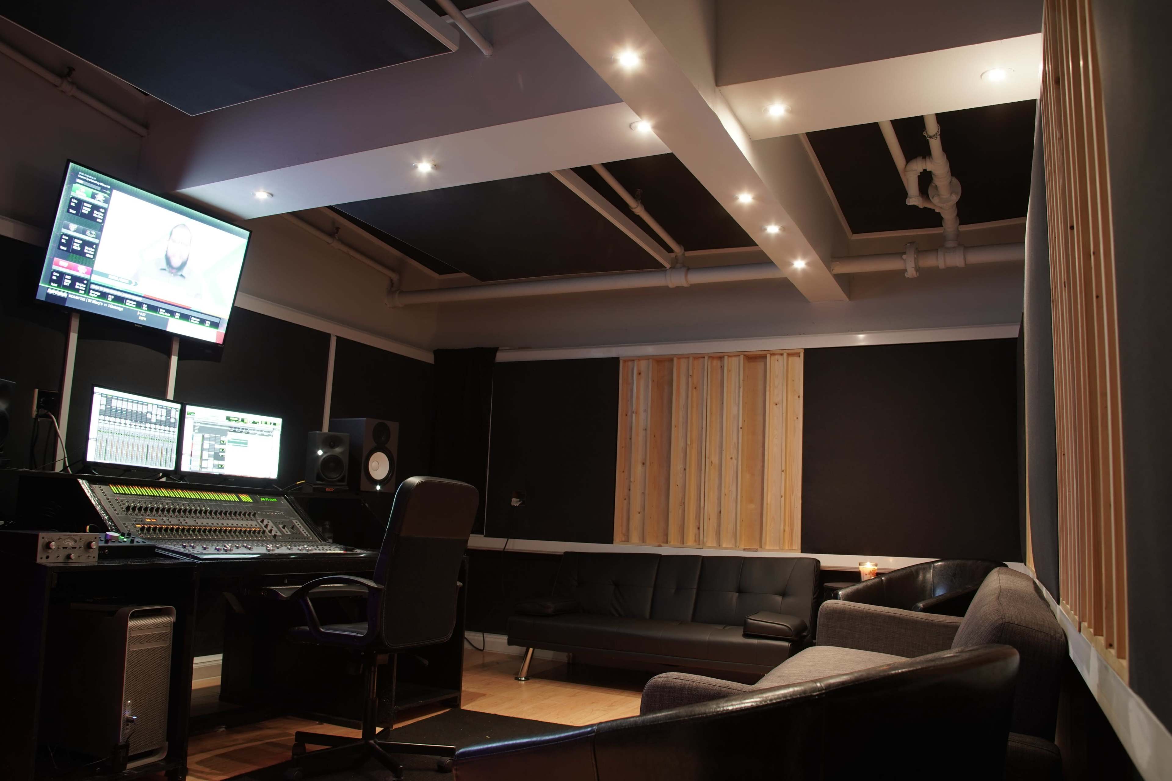 A modern recording studio featuring a sound mixing console, monitors, and a seating area with a black couch and chairs.
