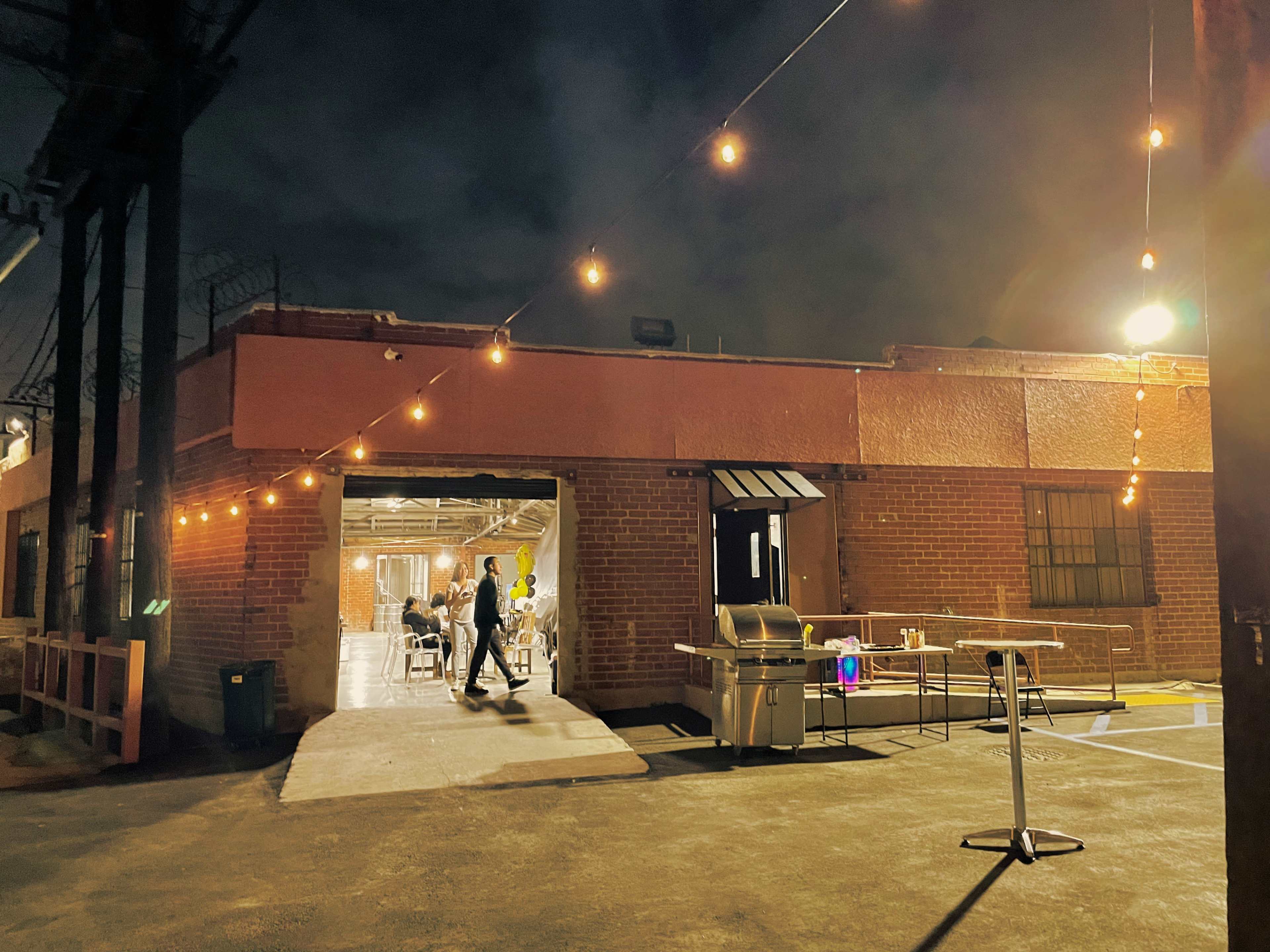 A person walks into a brick building with string lights illuminating the entrance on a dark night.