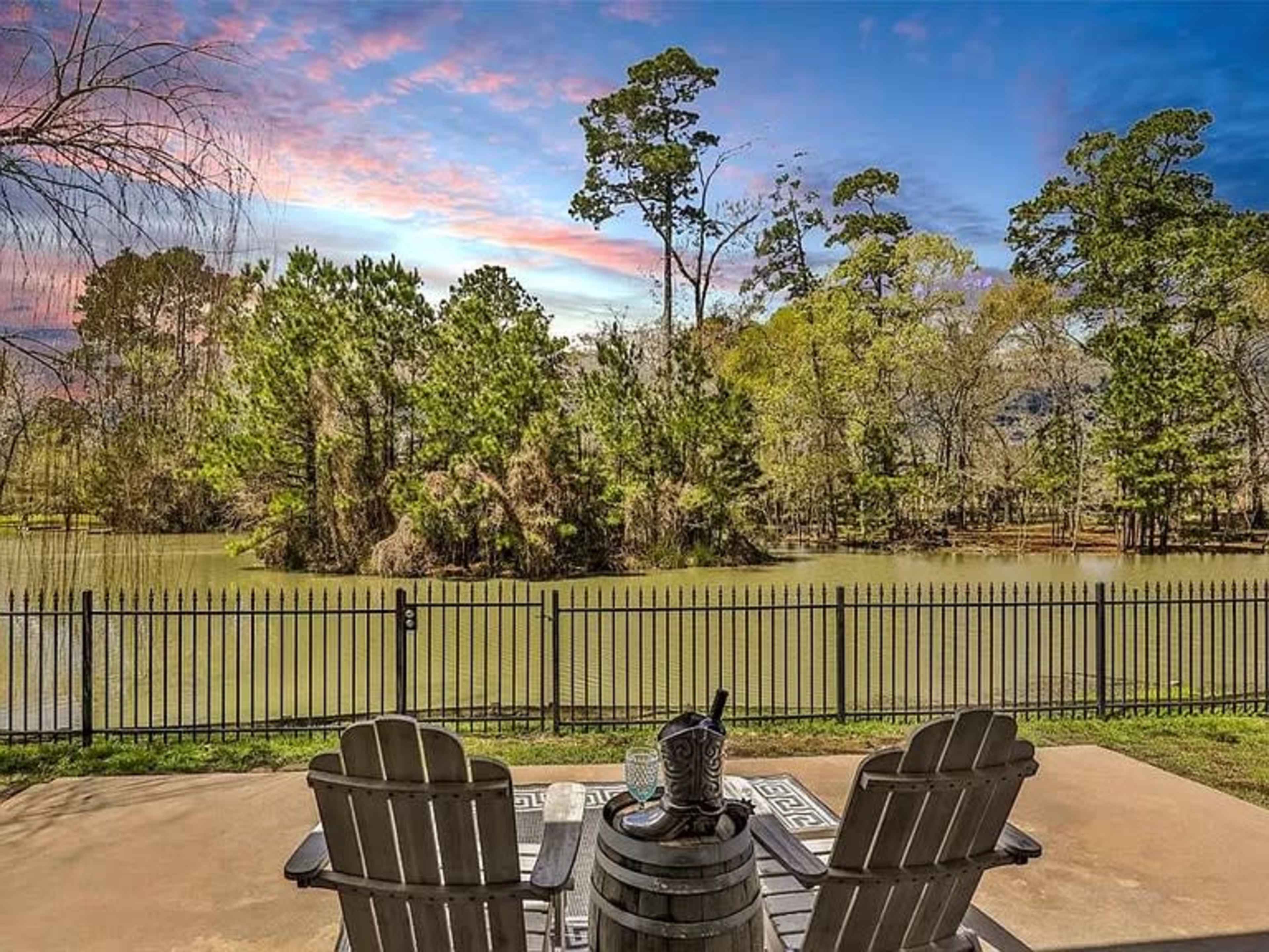 A patio with two chairs and a table overlooks a tranquil body of water surrounded by trees.