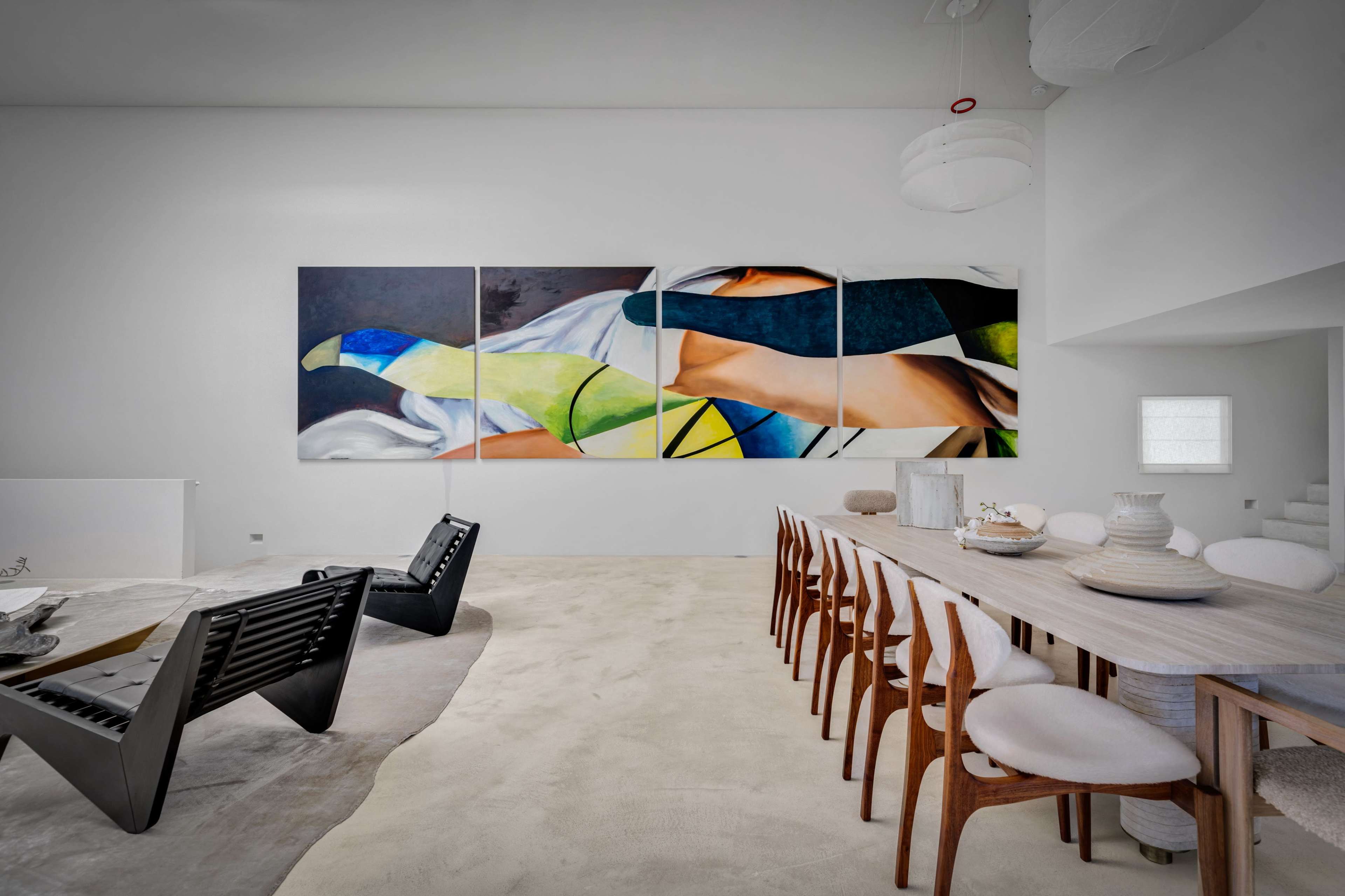 The image features a modern interior space with a dining table and chairs, black lounge chairs, and a large abstract artwork on the wall.