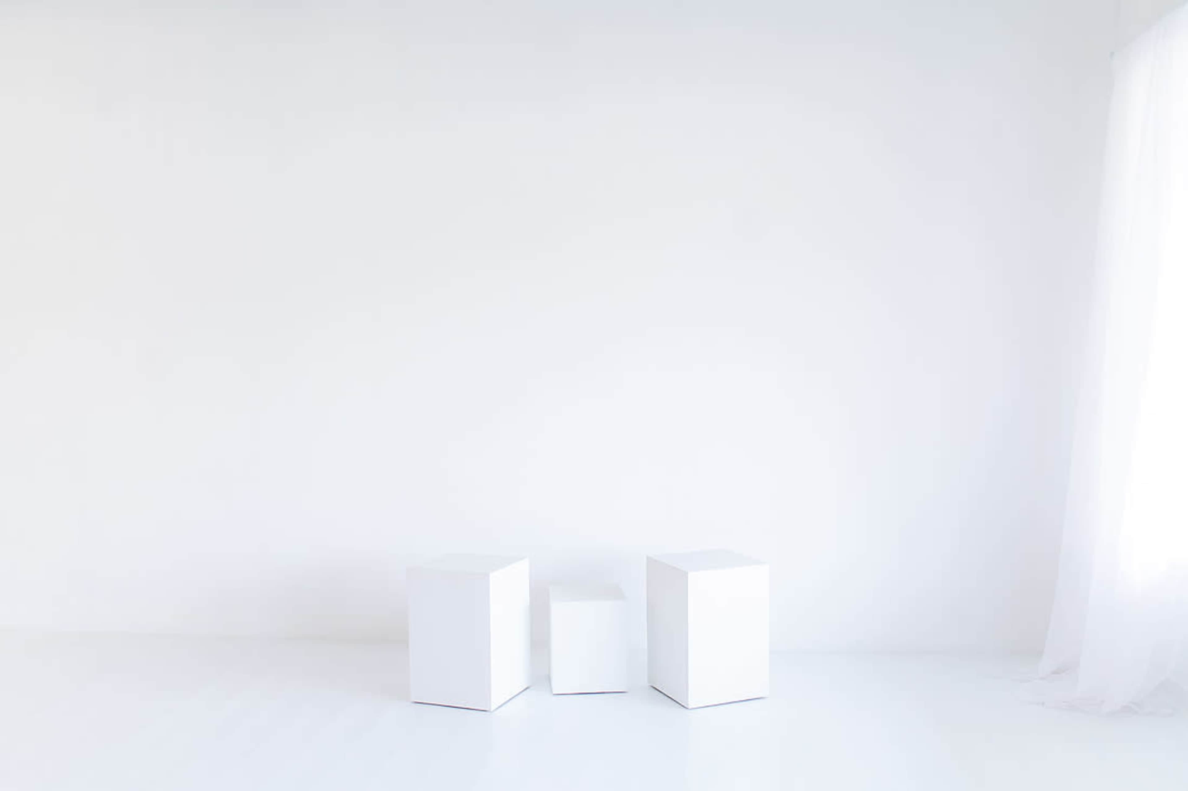 The image shows three white geometric boxes positioned on a white floor against a plain white wall.