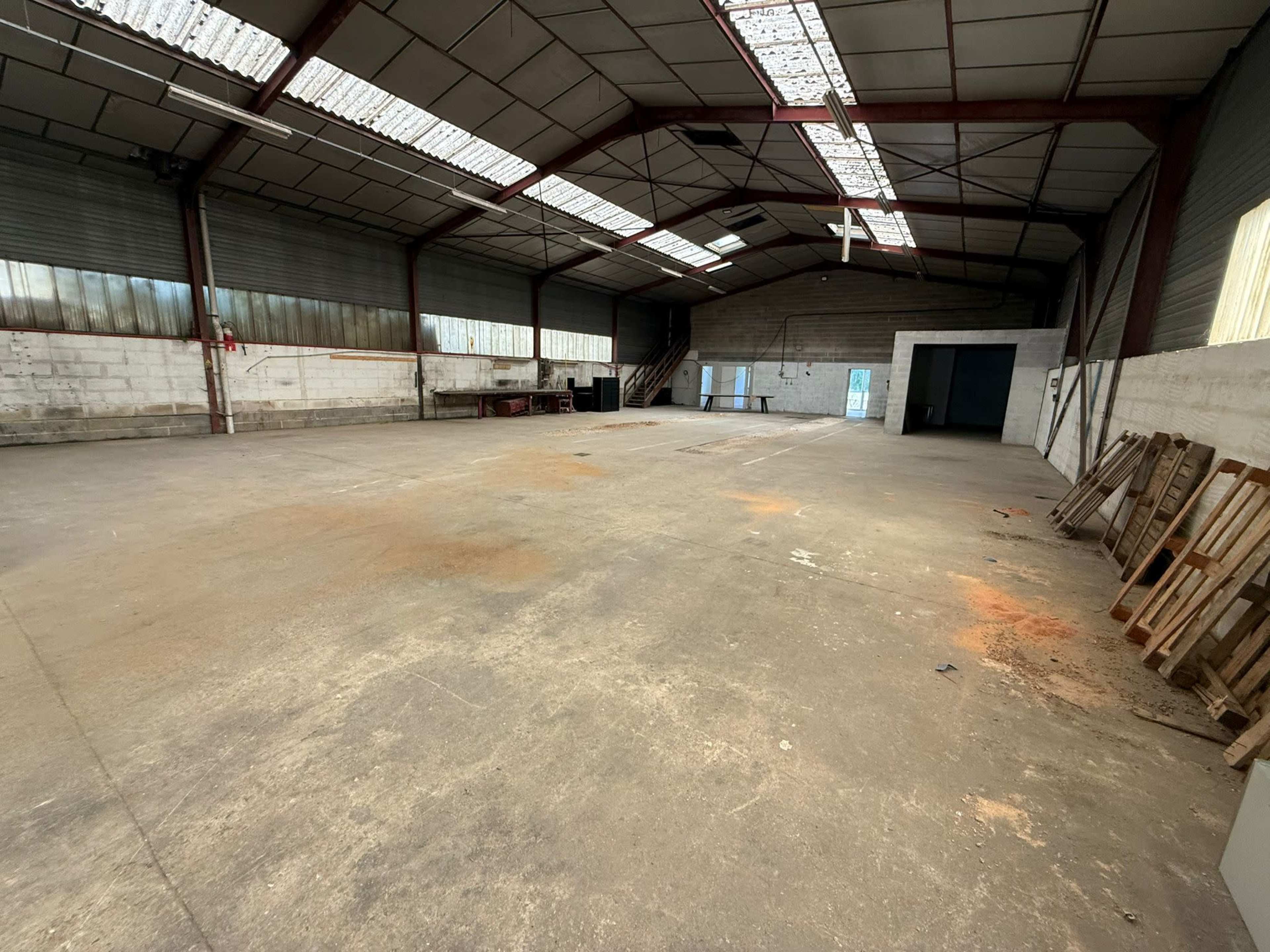 The image shows a spacious, empty warehouse with concrete flooring, high ceilings, and minimal equipment along the walls.