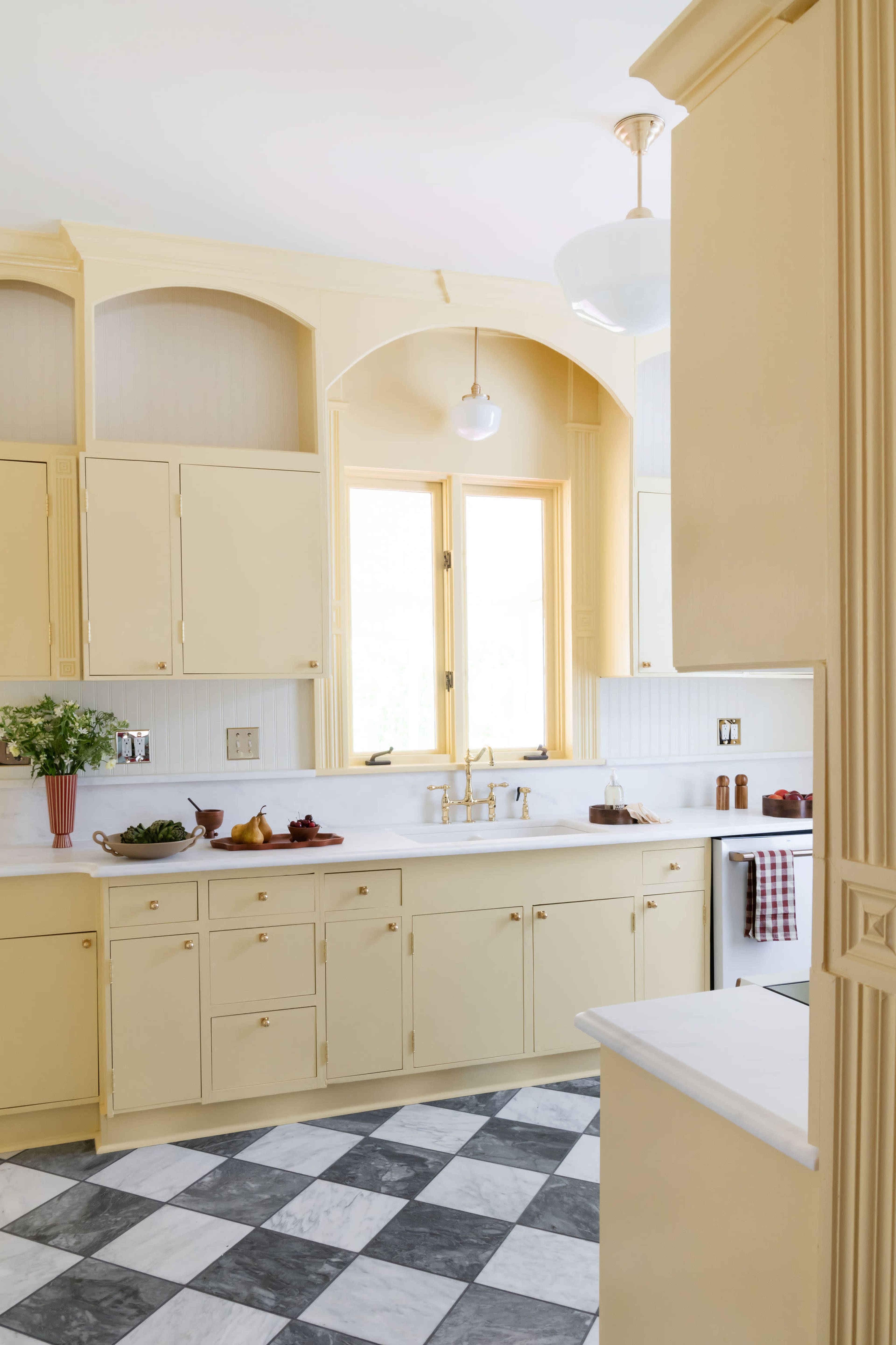 The image shows a bright kitchen featuring yellow cabinetry, a marble countertop, and a checkered floor.