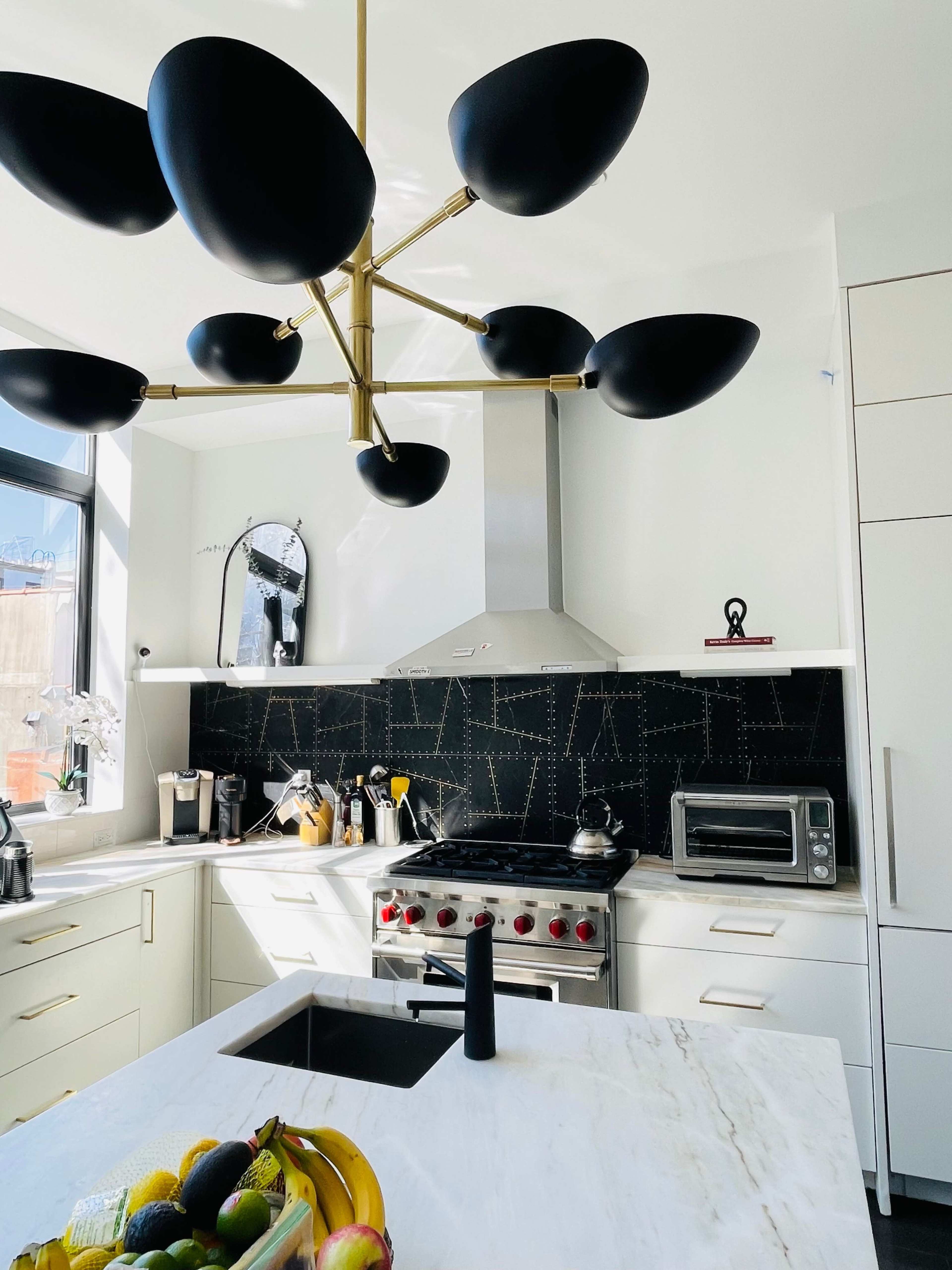 The kitchen features a central black chandelier, stainless steel appliances, and a marble countertop with a fruit bowl.