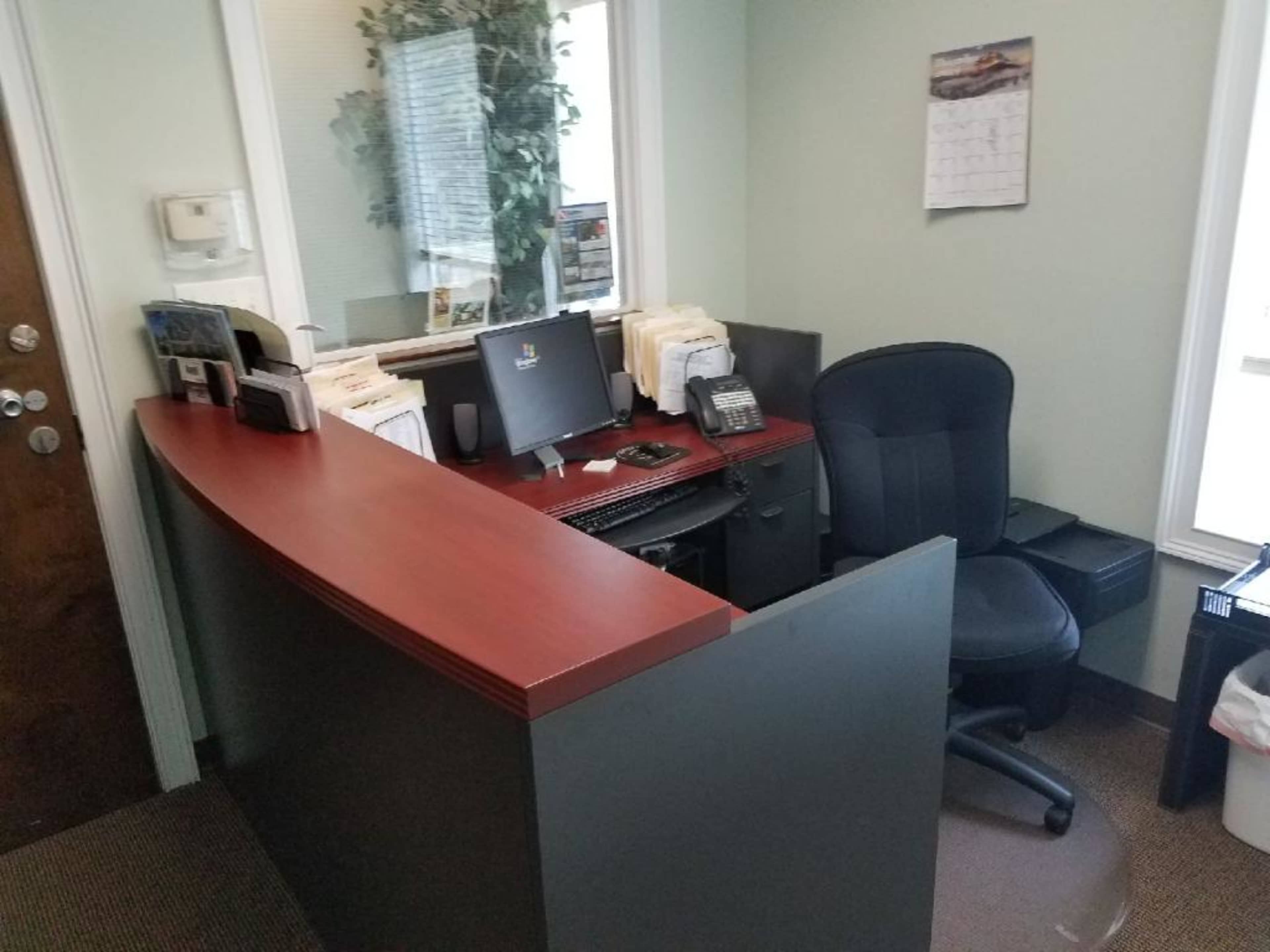 A reception area with a wooden front desk, a computer, a chair, and organized files on the counter.