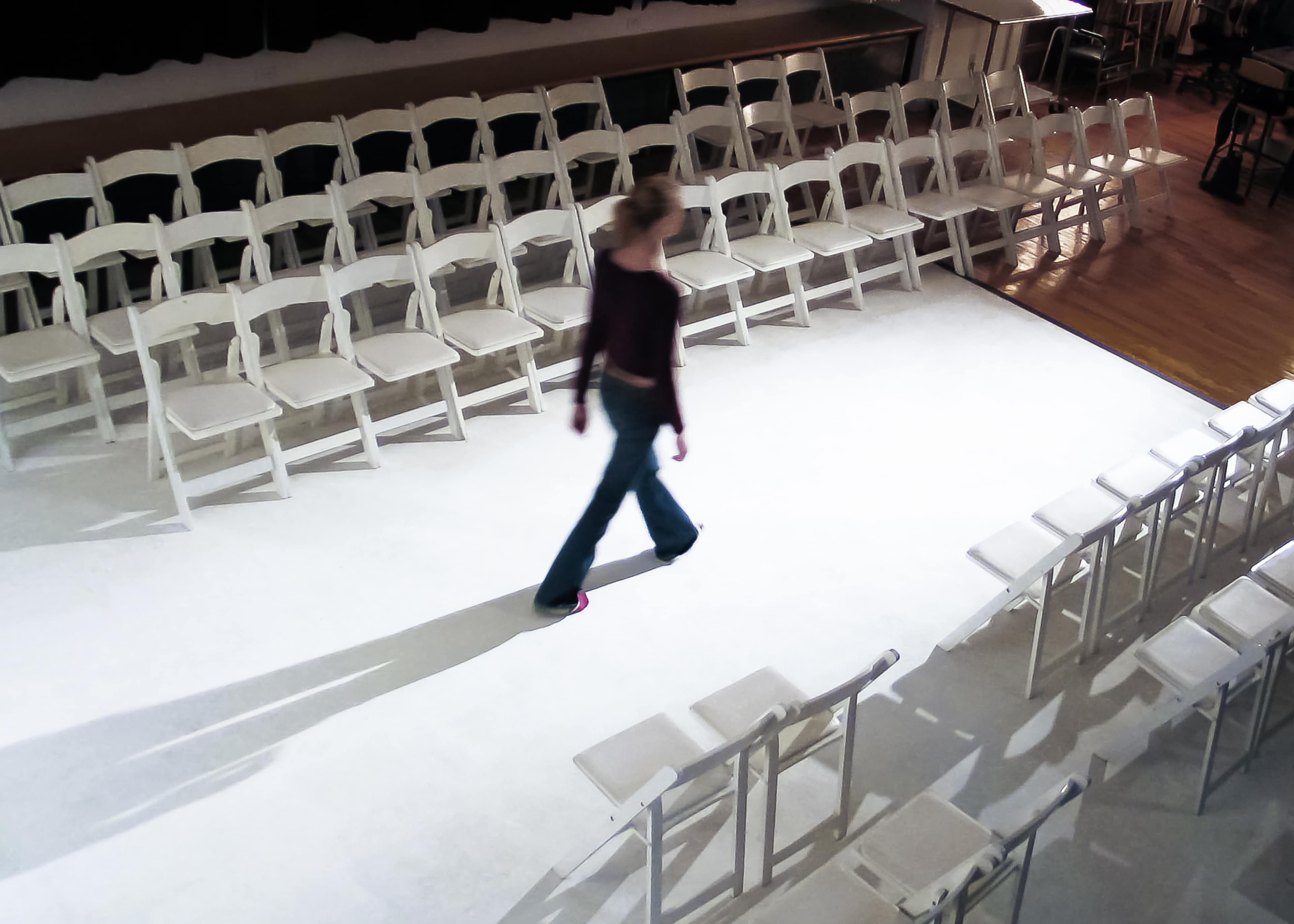 A person walks along a runway surrounded by multiple rows of white chairs.