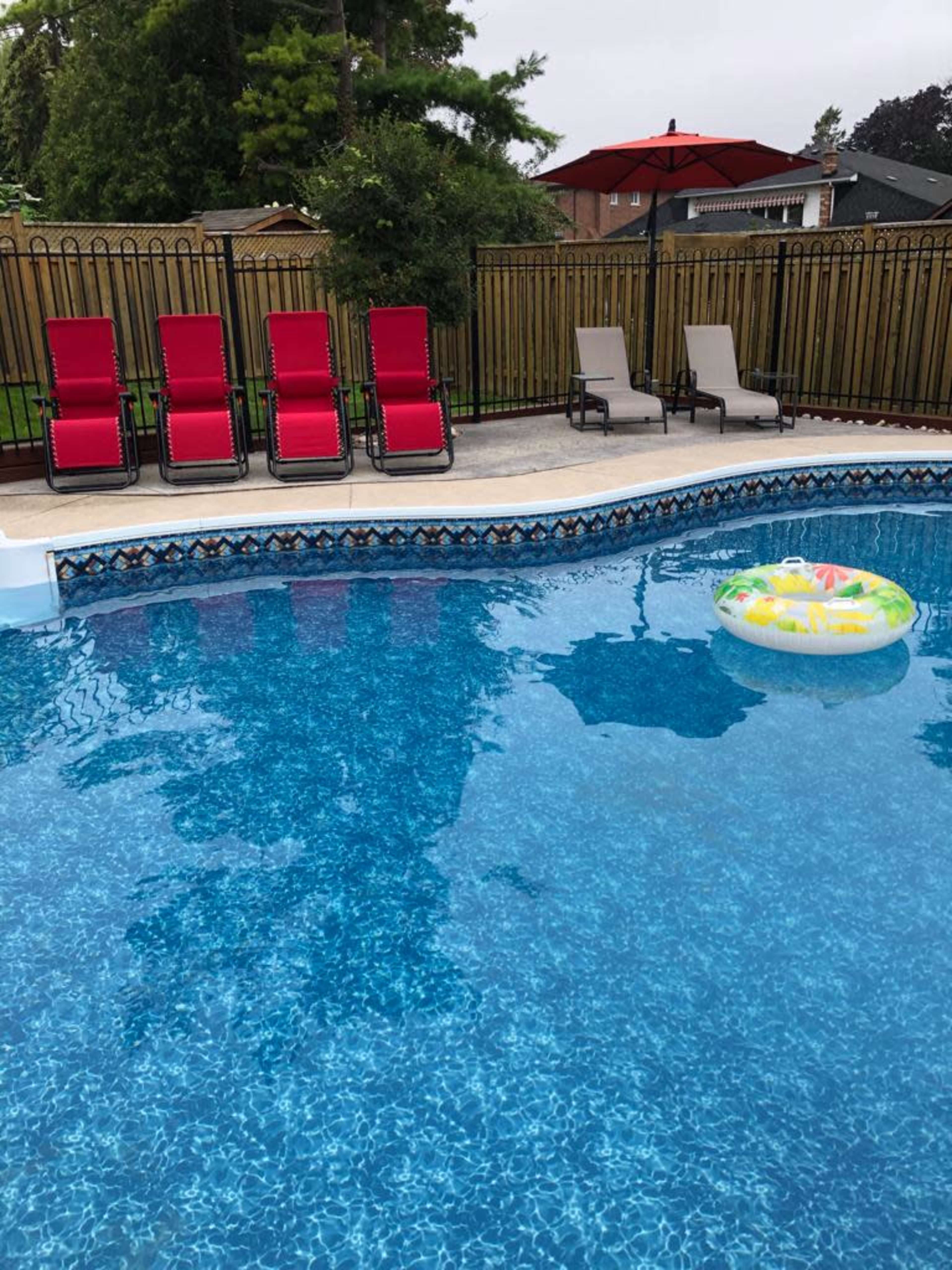 A swimming pool with bright blue water, surrounded by several lounge chairs, an umbrella, and a float in the water.