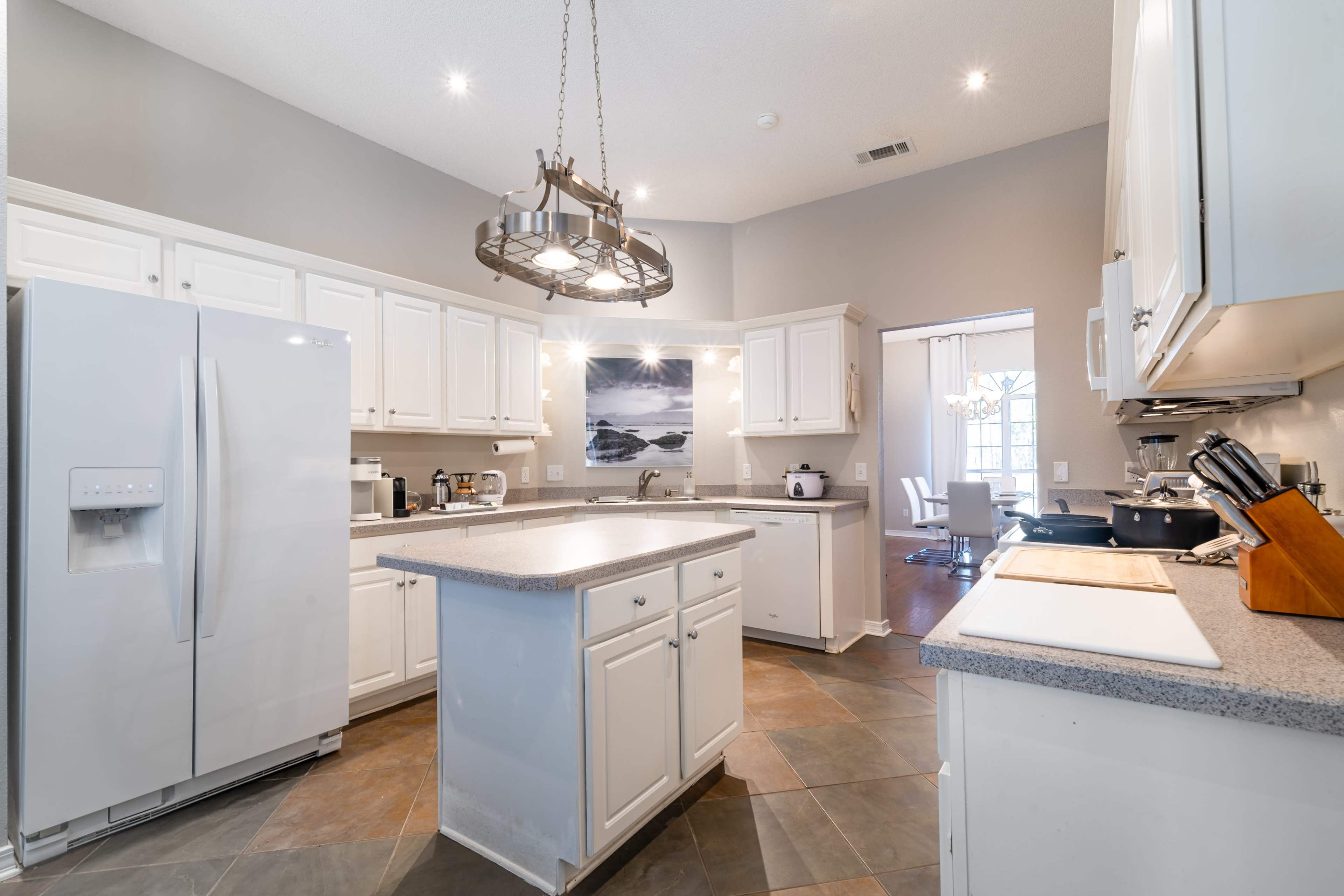 A modern kitchen features white cabinetry, a central island, and stainless steel appliances with a view into an adjacent dining area.
