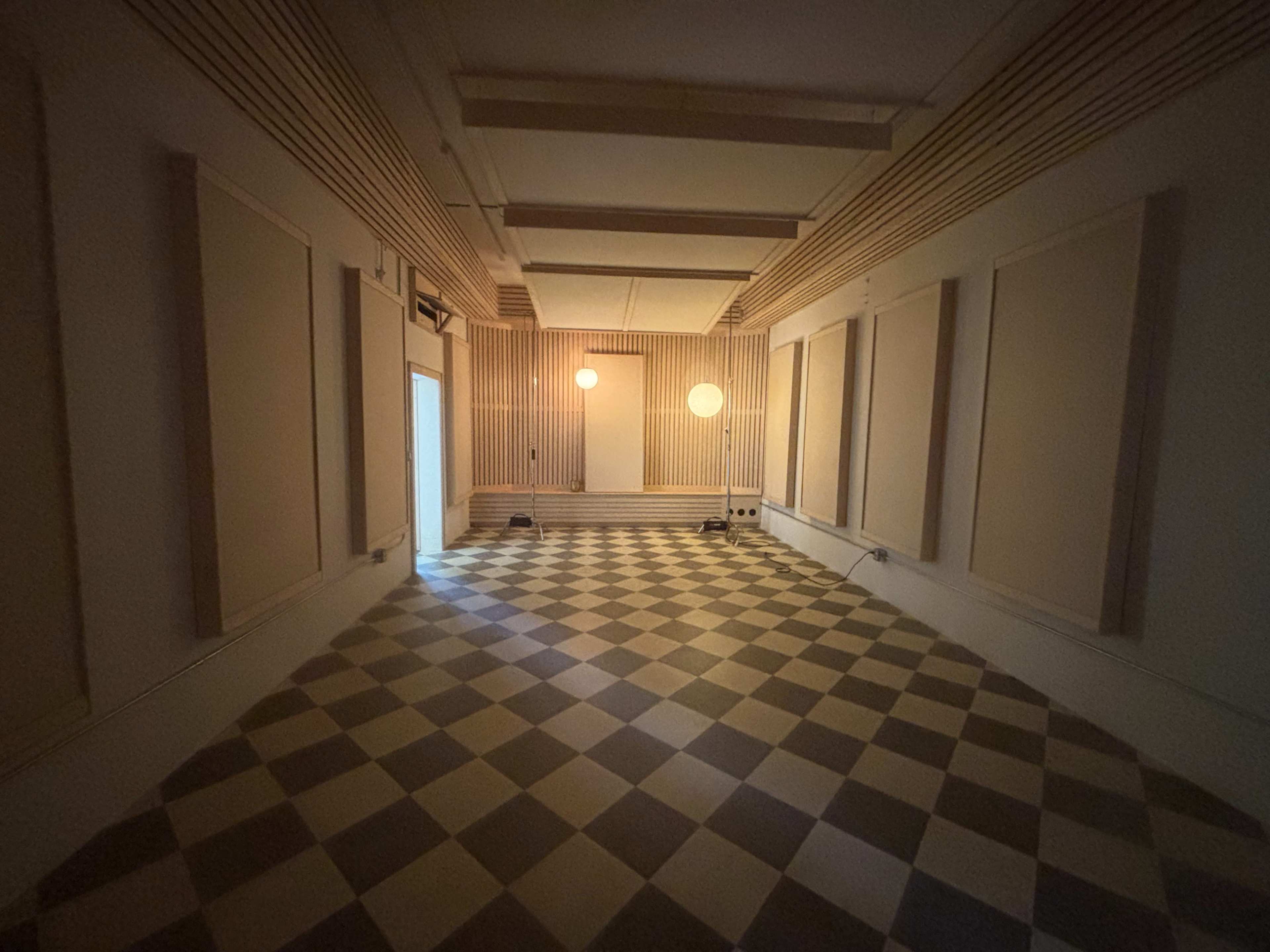 The image shows a spacious, rectangular room with checkered flooring and two round light fixtures on the walls.